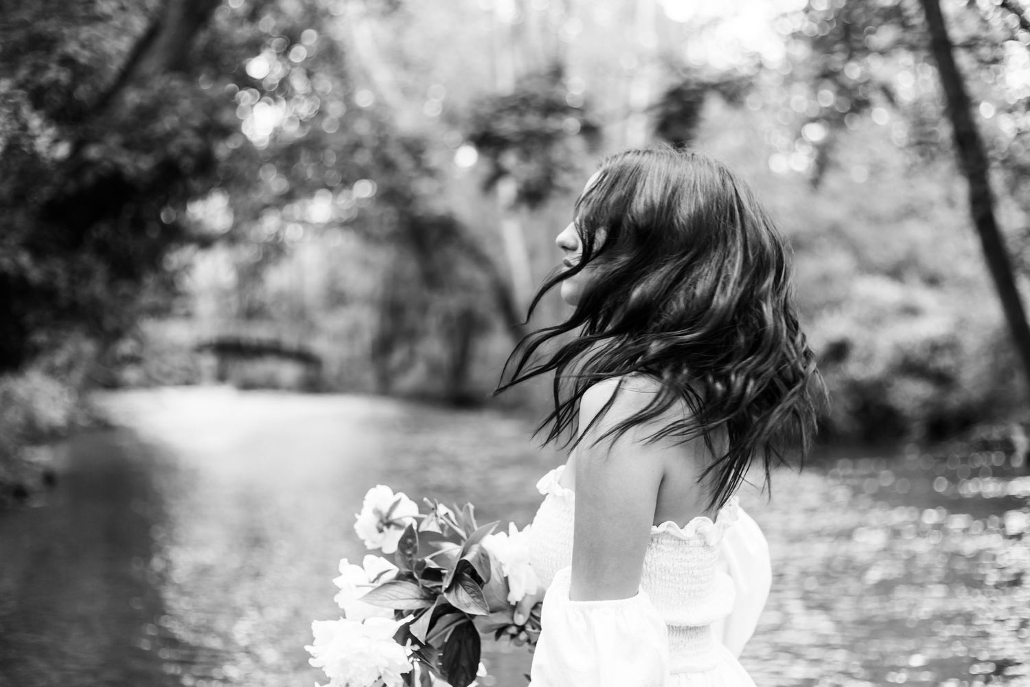 Black and white artistic portrait with closed eyes and flowing hair beside white flowers in soft focus.