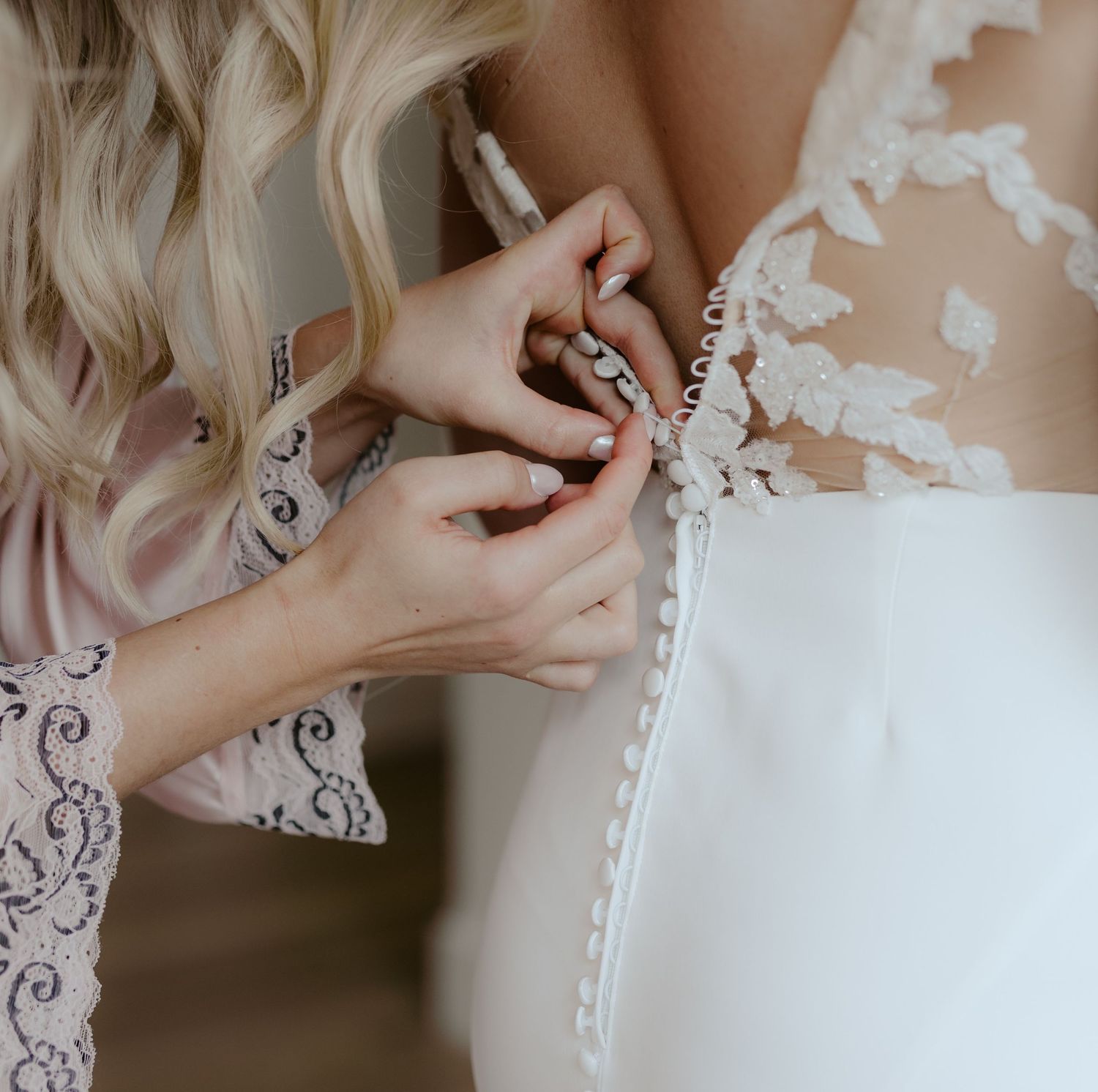 Hands delicately adjusting the lace and buttons on an elegant white wedding dress with intricate floral detailing.