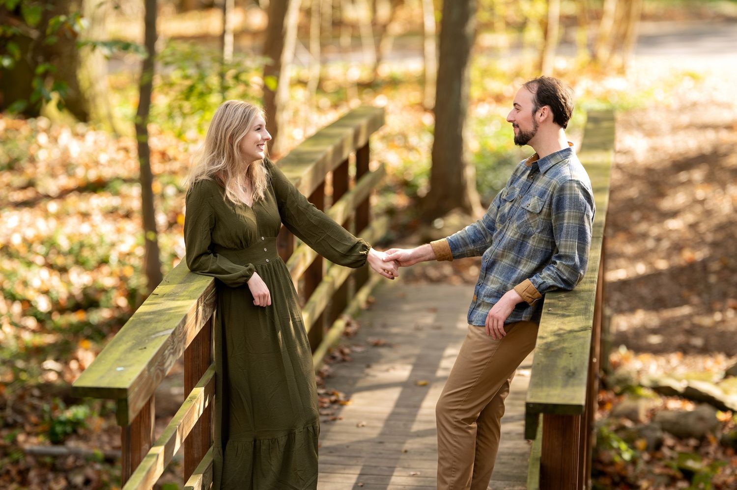 Couple holding hands on wooden bridge surrounded by fall foliage in forest park.