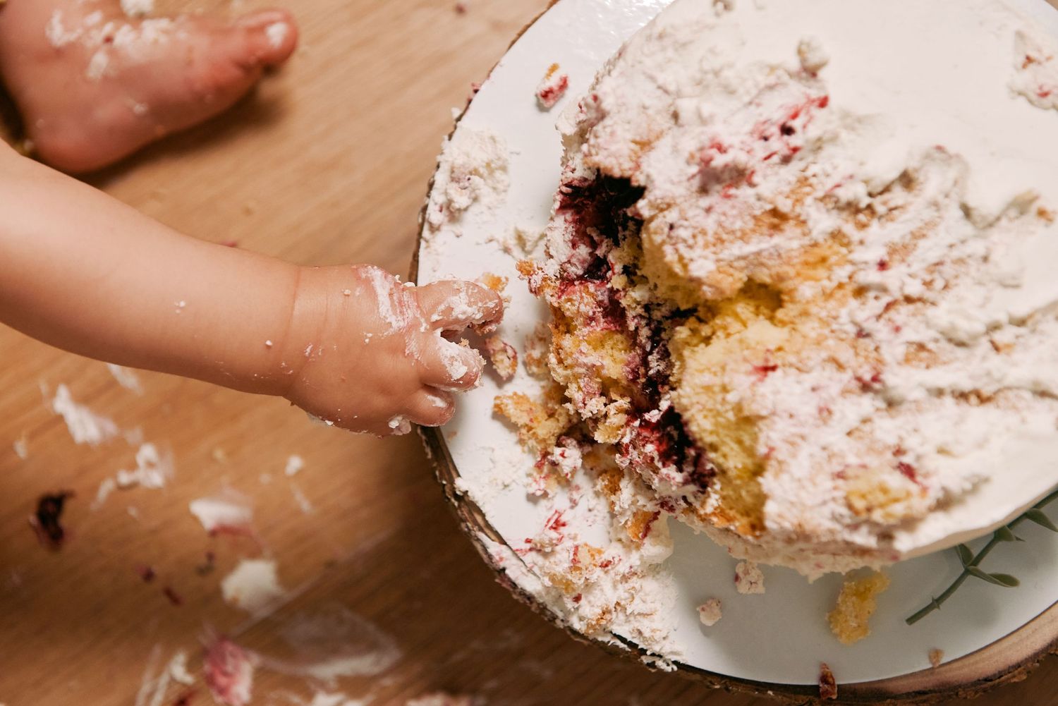 Baby hand smashing into white frosted birthday cake on wooden table.