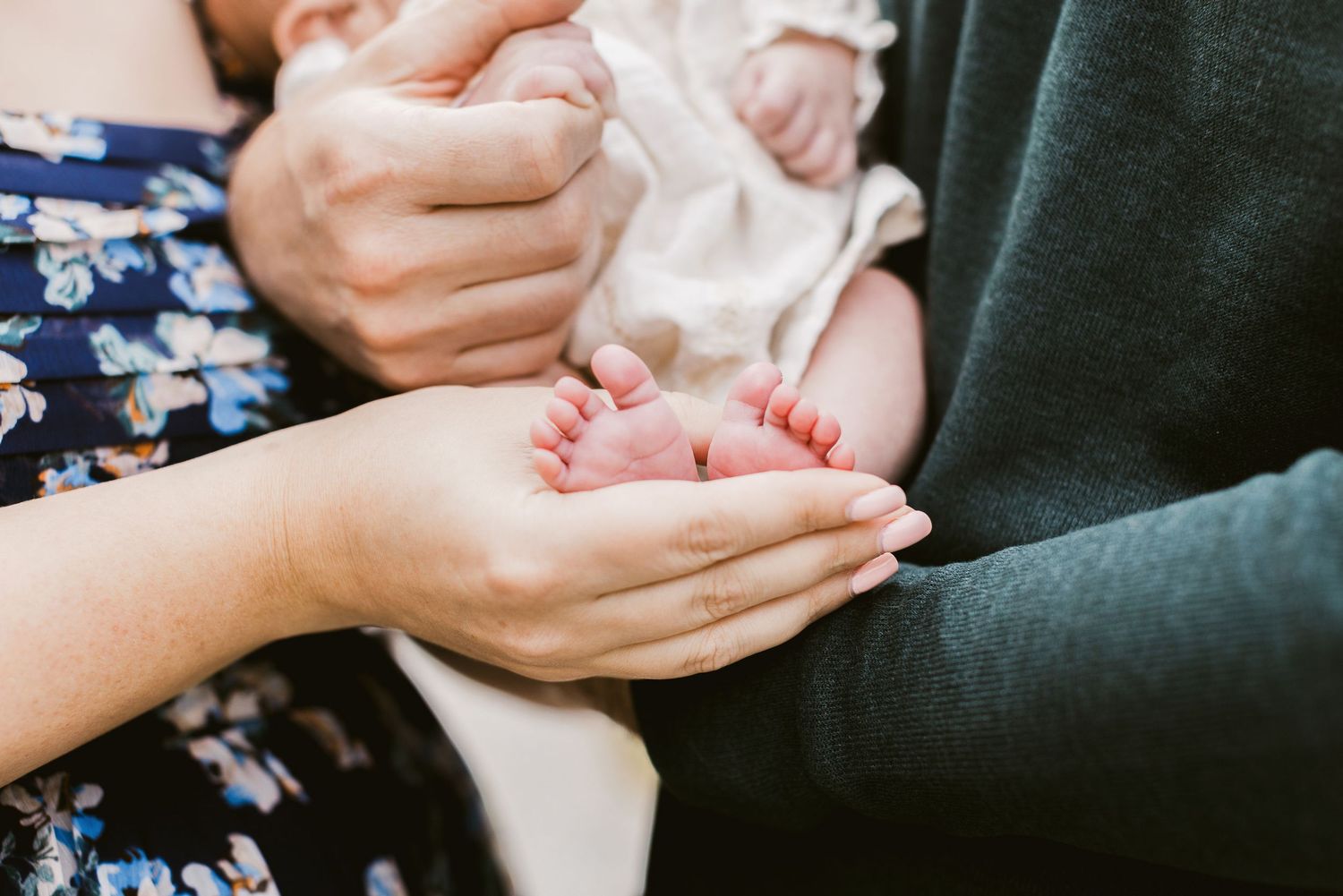 A mother wearing a floral navy blue dress and husband a green sweater, hold their newborn baby girl wearing a cream outfit in Tamworth, NH.