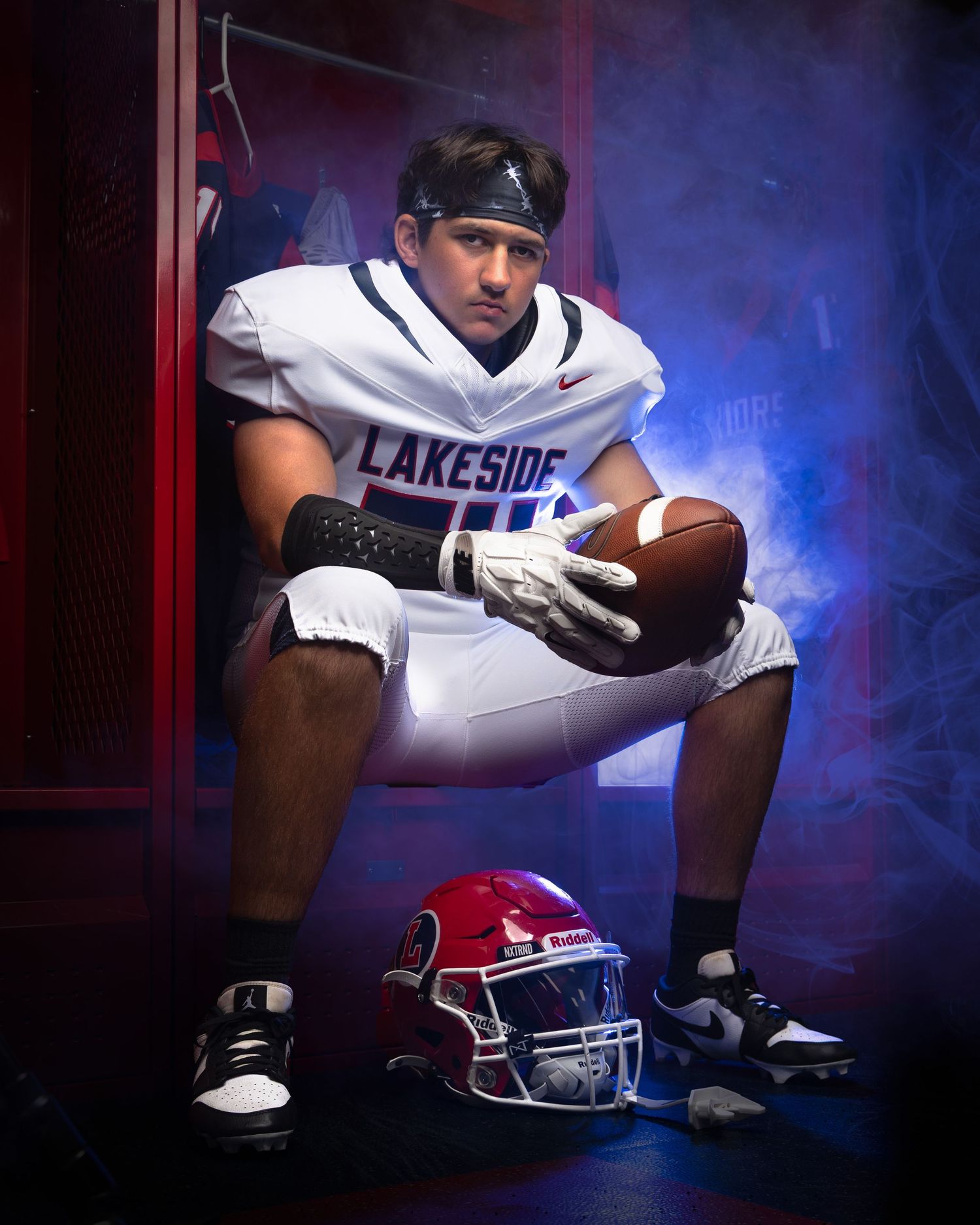 Football player in white uniform and black helmet crouches in dramatic lighting with red and blue smoke effects.