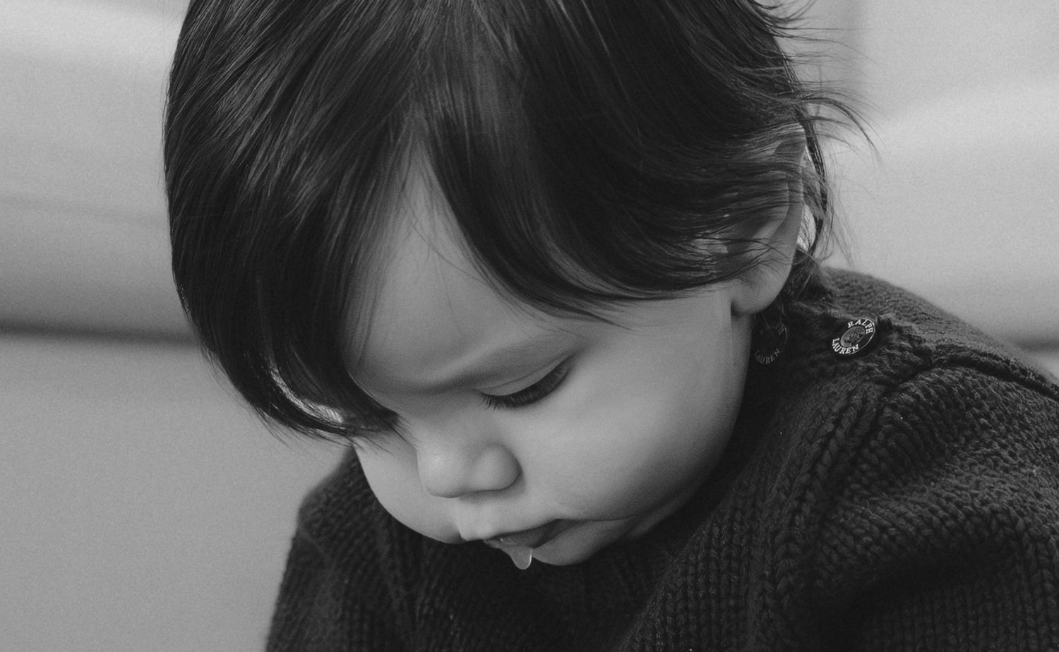 A young child in a black sweater looks down thoughtfully in this black and white portrait.