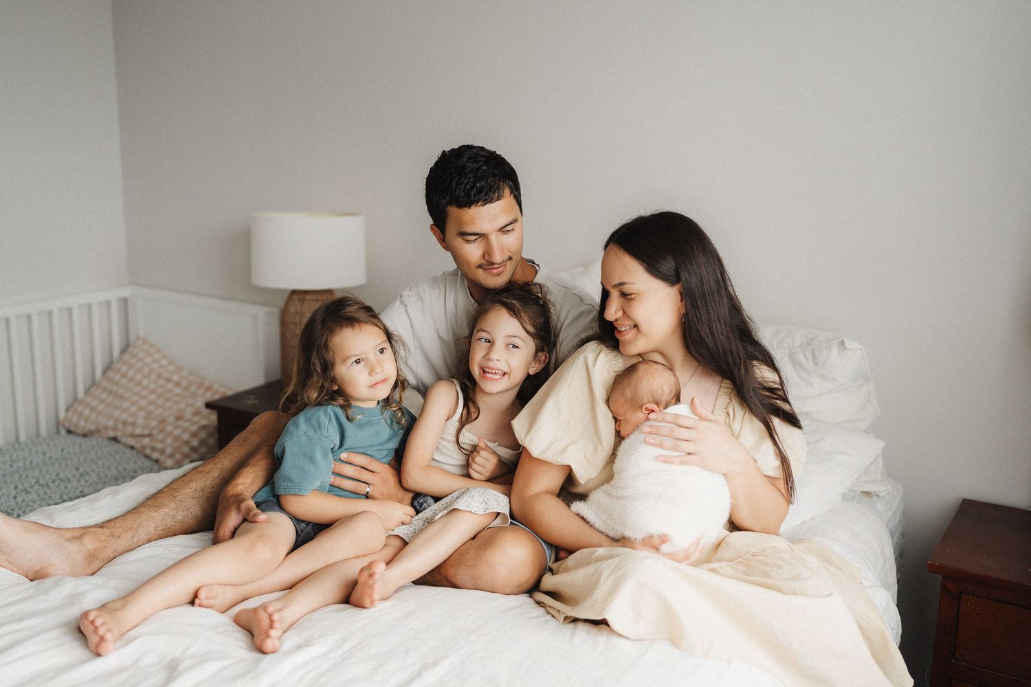 Family snuggling together in white bedding while enjoying relaxed morning moments at home.