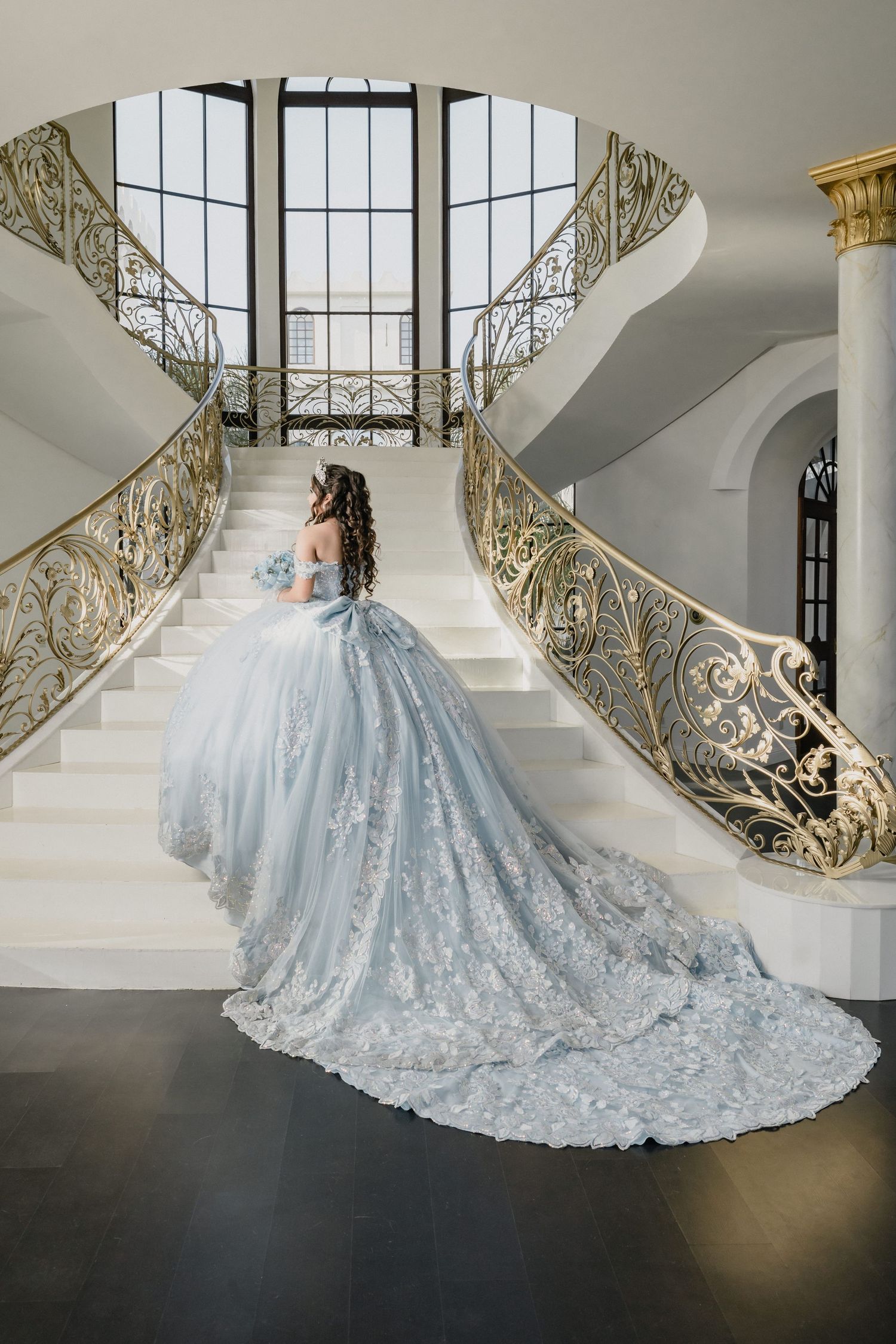 Elegant light blue ball gown with intricate lace details cascades down grand staircase in luxurious venue.
