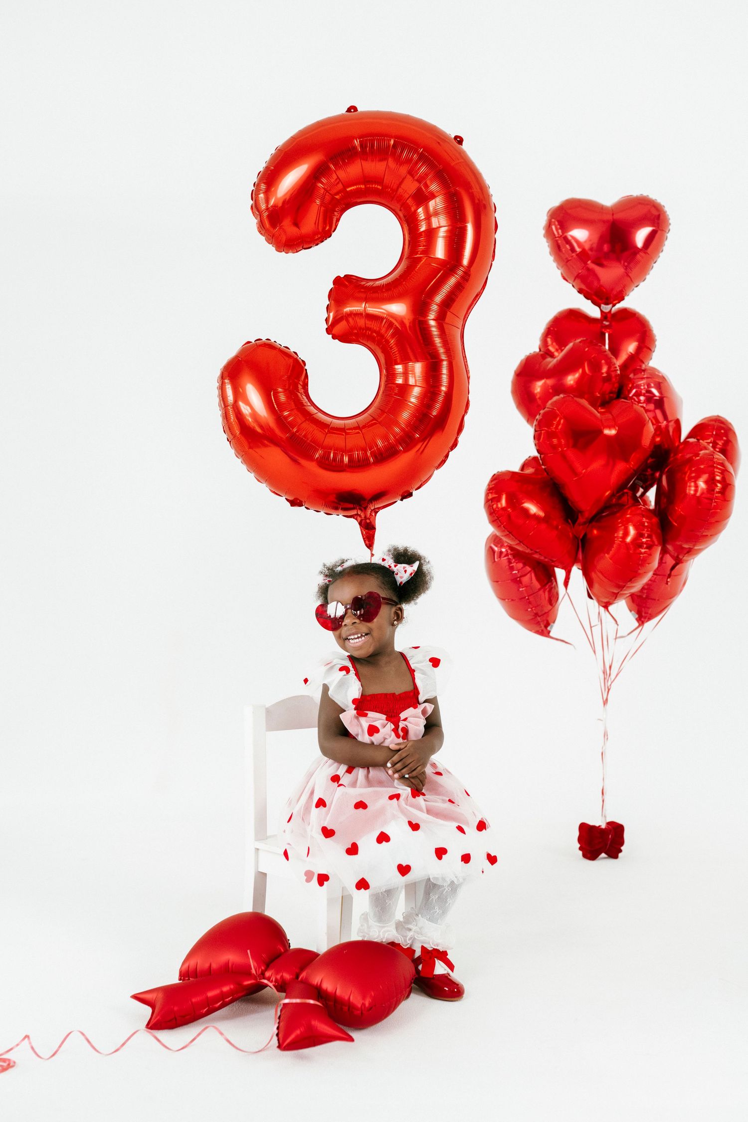 Red number 3 balloon and heart-shaped balloons create festive Valentine's Day scene with white and red heart dress.
