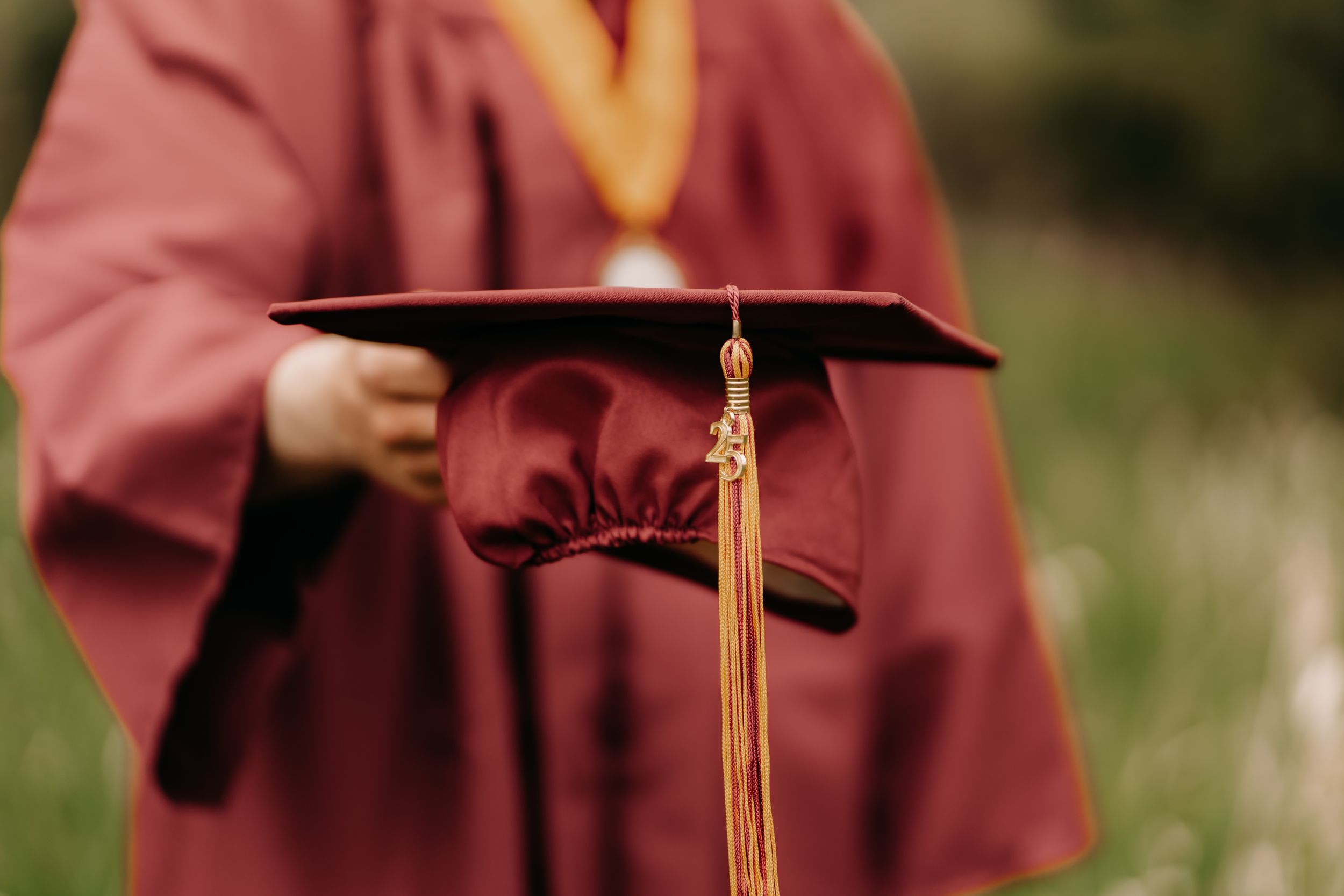 A high school graduate in burgundy cap and gown during an outdoor senior cap and gown photo session in Puyallup.