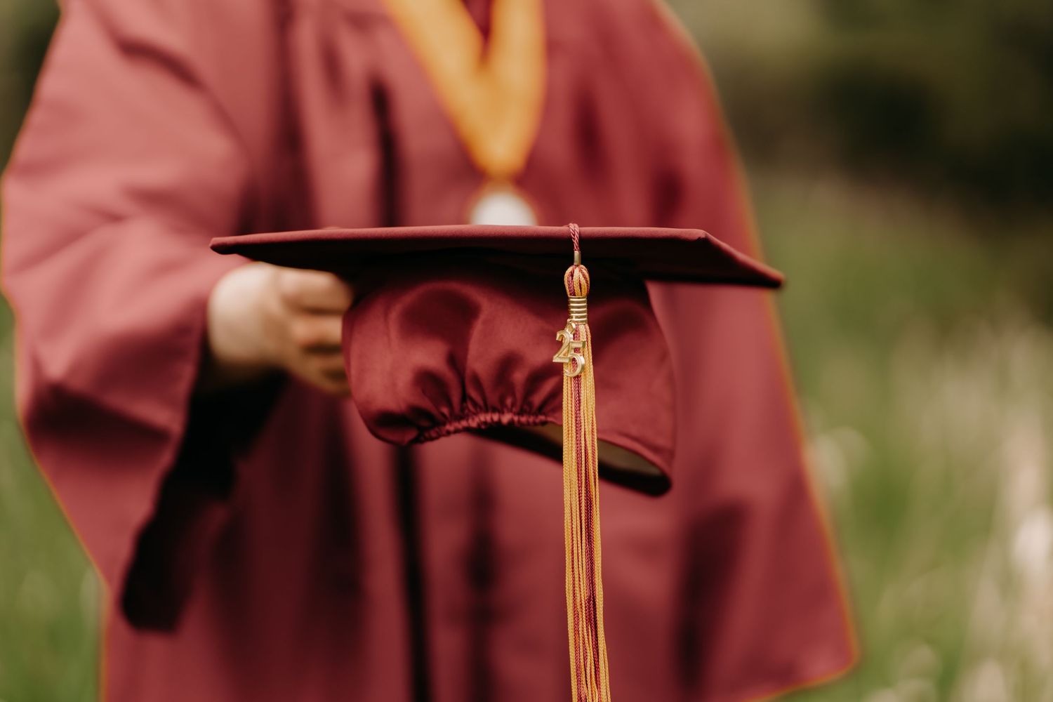 A high school graduate in burgundy cap and gown during an outdoor senior cap and gown photo session in Puyallup.