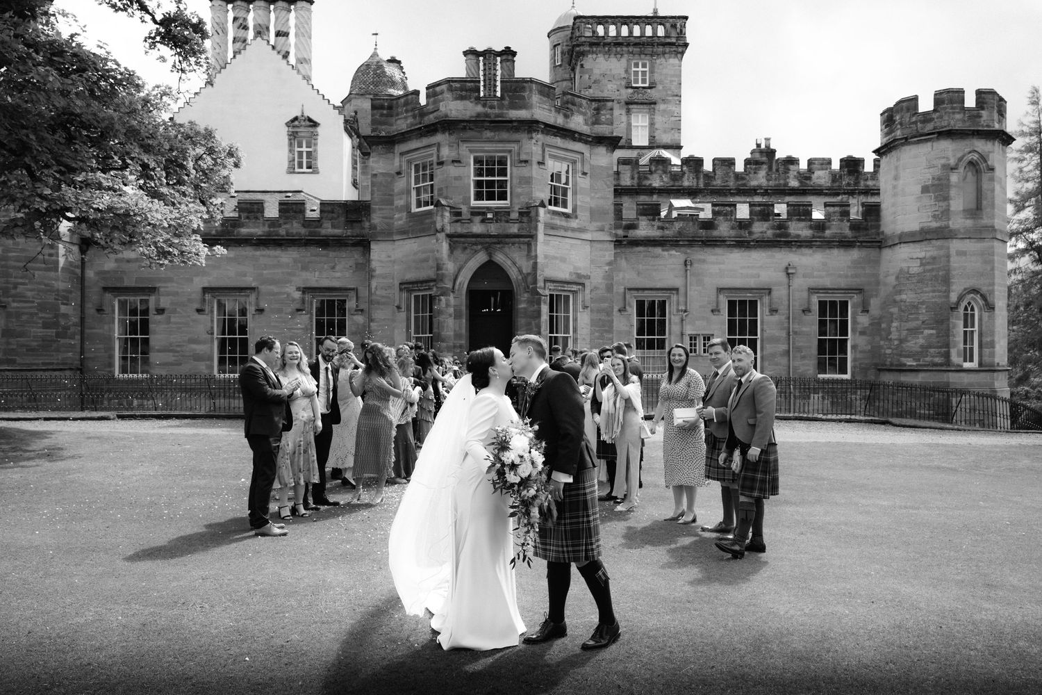 Couple walking through a garden path in wedding attire on a rainy day with umbrellas.