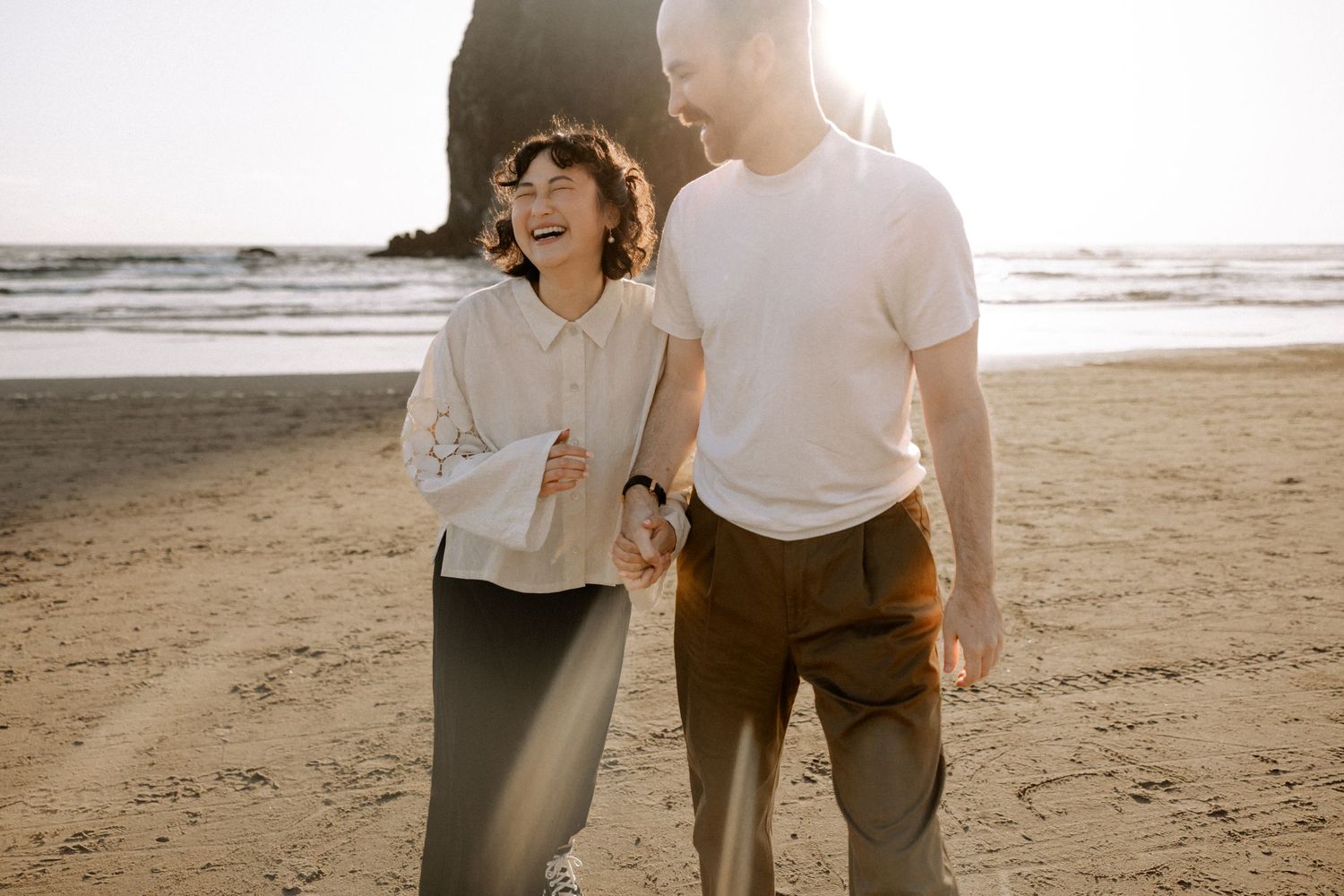 A couple walks hand in hand along a serene beach at sunset creating romantic silhouettes against the golden sky.
