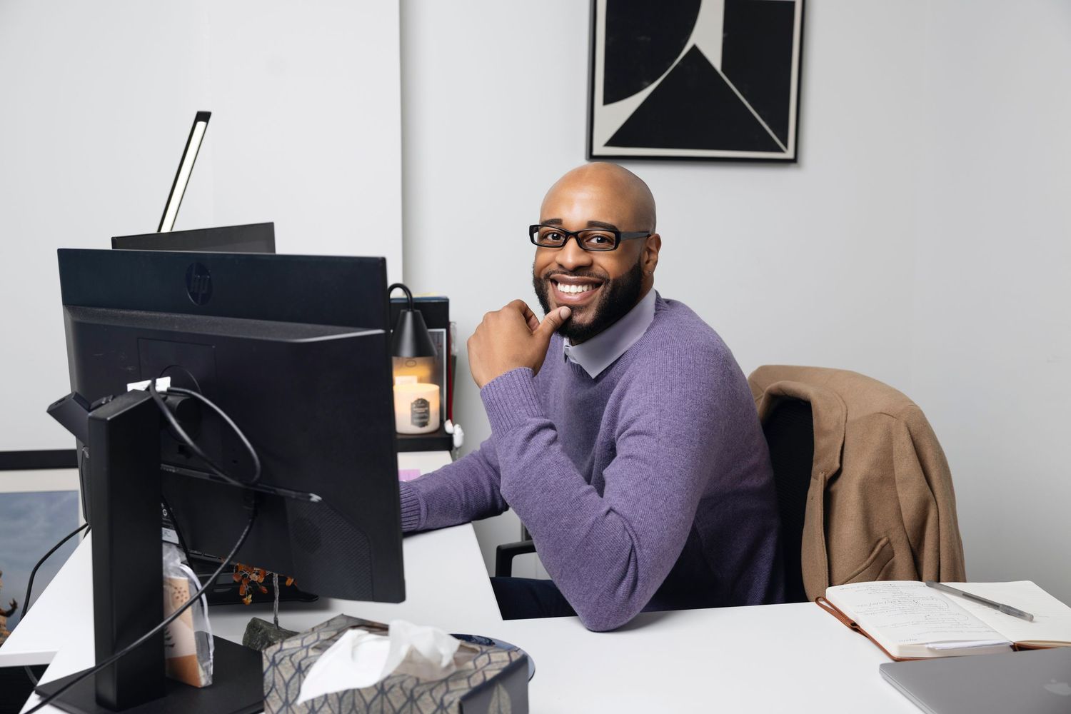 Professional in a purple sweater works at a desk with multiple computer monitors in a modern office setting.