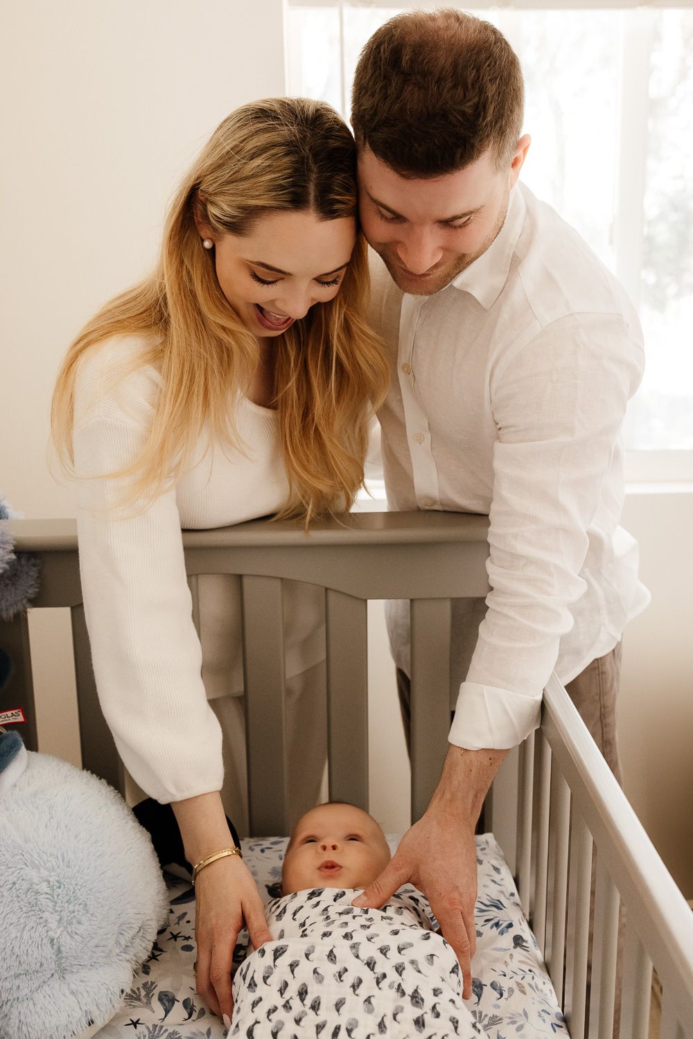 Parents smile while looking at their newborn baby in his crib at Bay Area in-home newborn photography session