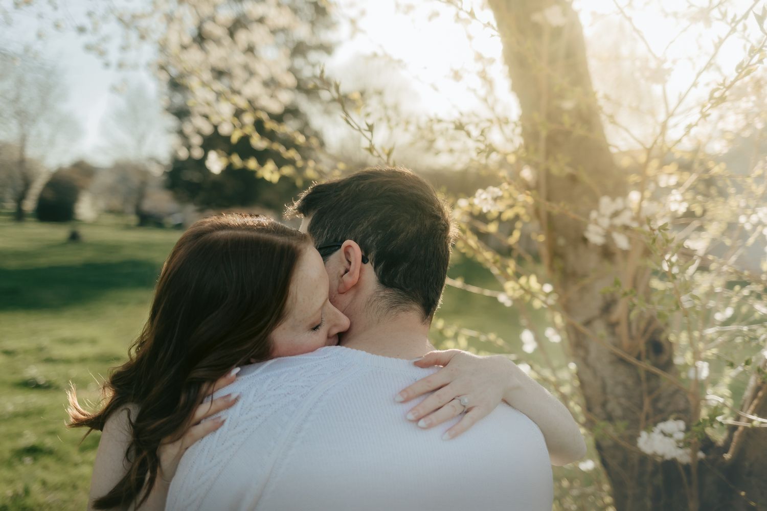 Couple embracing under sunlit spring blossoms, authentic connection at a small intimate Mercer County Park elopement in New Jersey