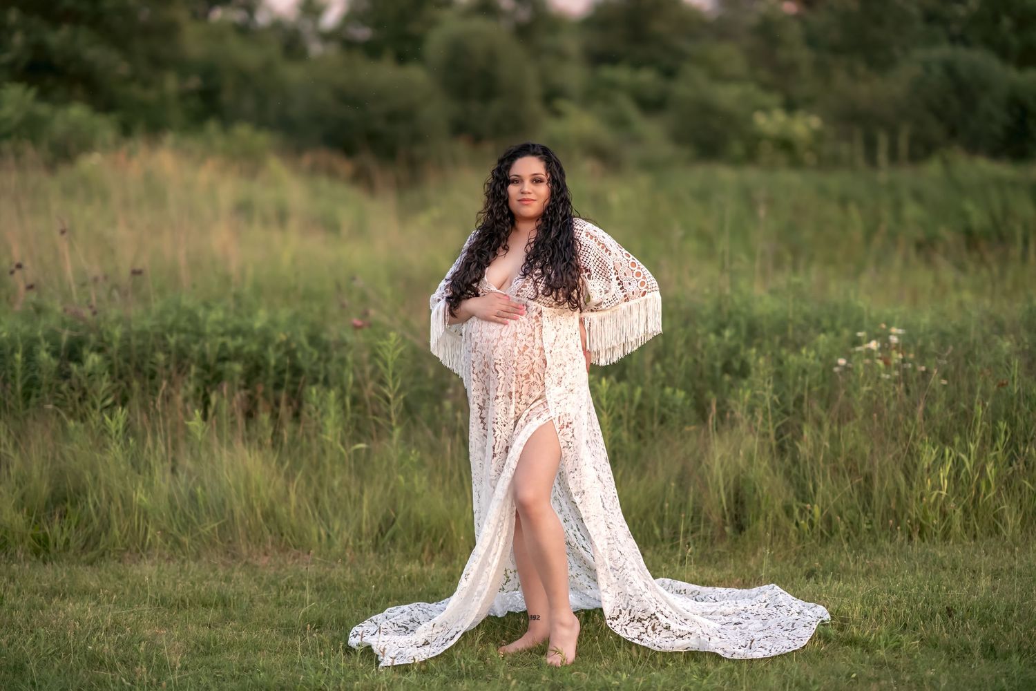 A person in a flowing white lace dress walks through a green summer meadow at golden hour.