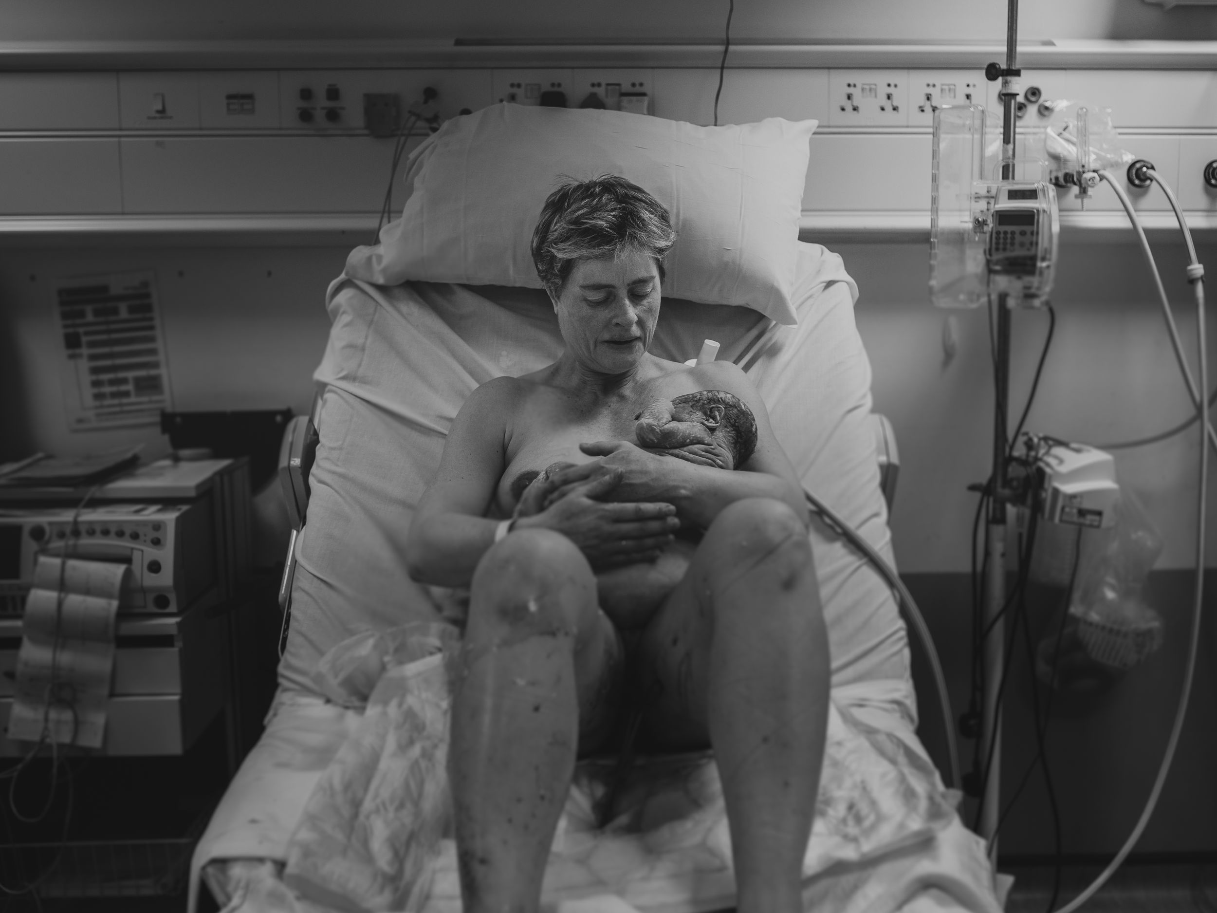 A mother holding her newborn baby for the first time, moments after birth, with blood and vernix still visible —birth photographer beckenham