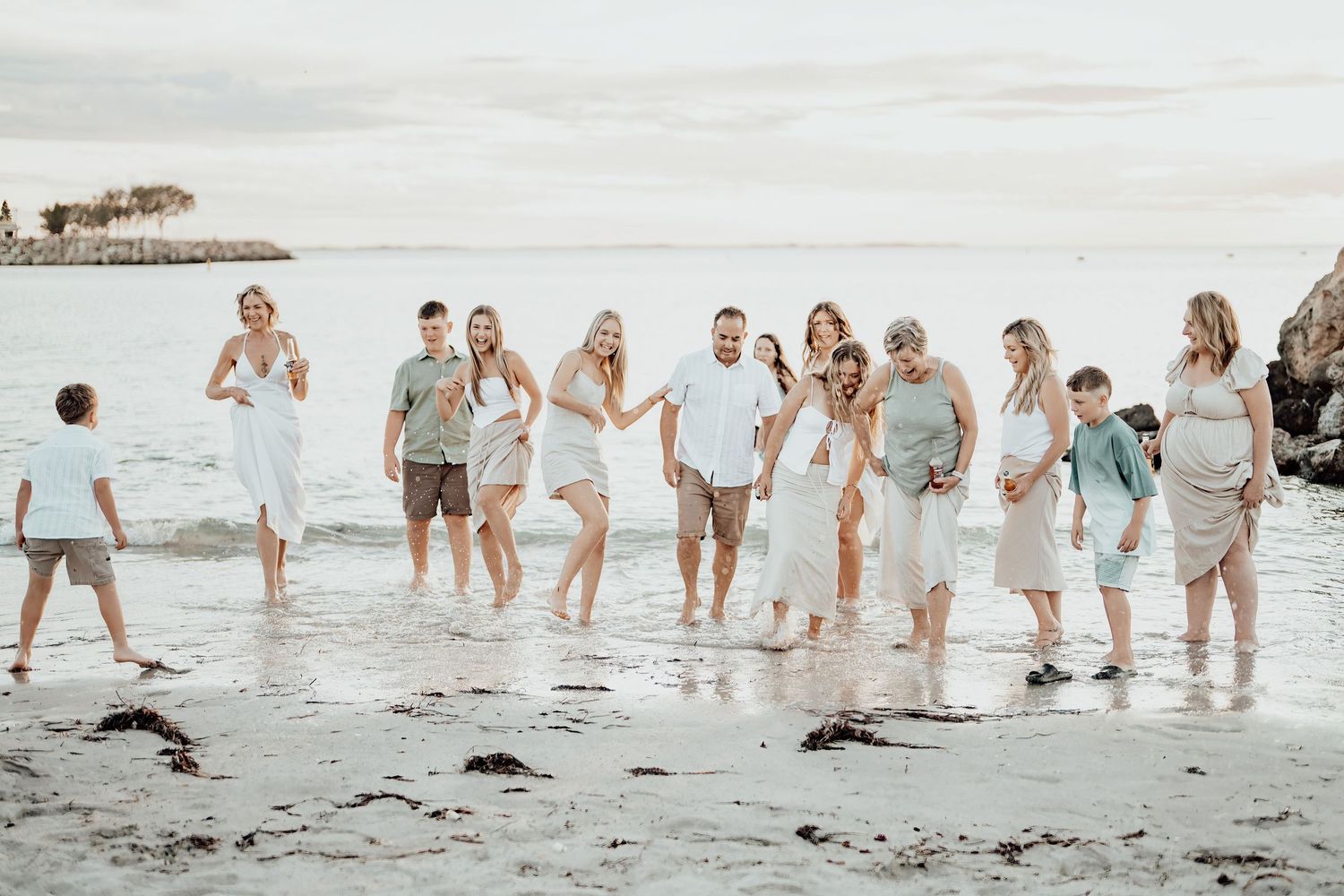 Group of people walking along the shoreline at sunset enjoying a beach photoshoot in light colored outfits.