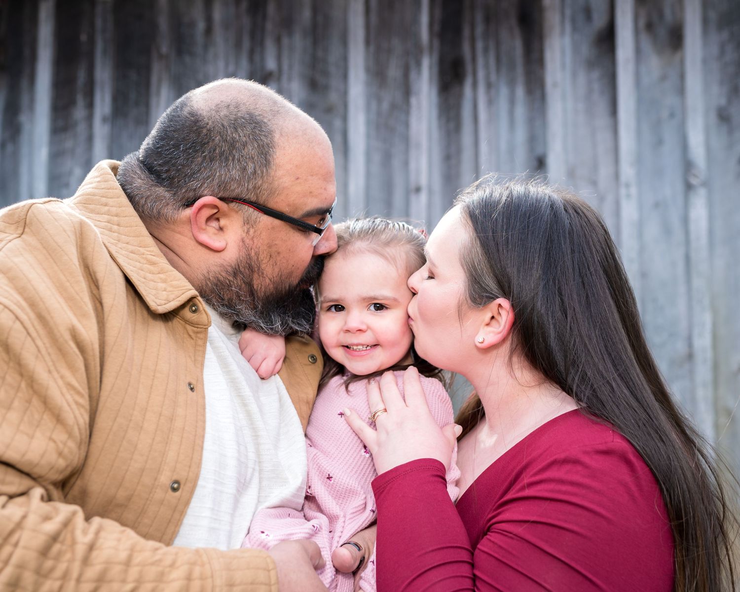 A family of three shares tender moments together in a series of connected outdoor photos against a wooden fence.