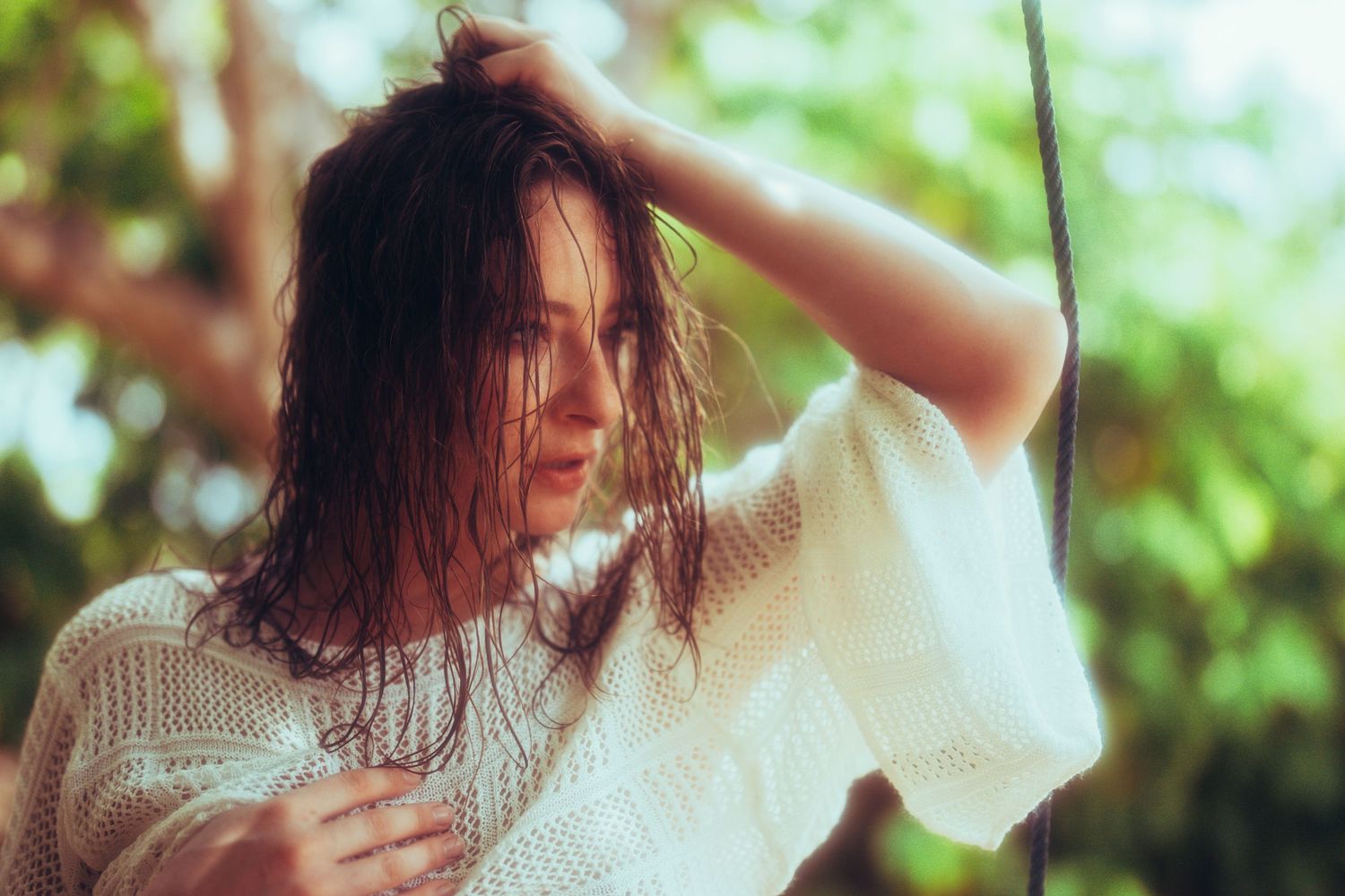 Woman with long dark hair in white sweater dancing with raised arms in natural lighting.