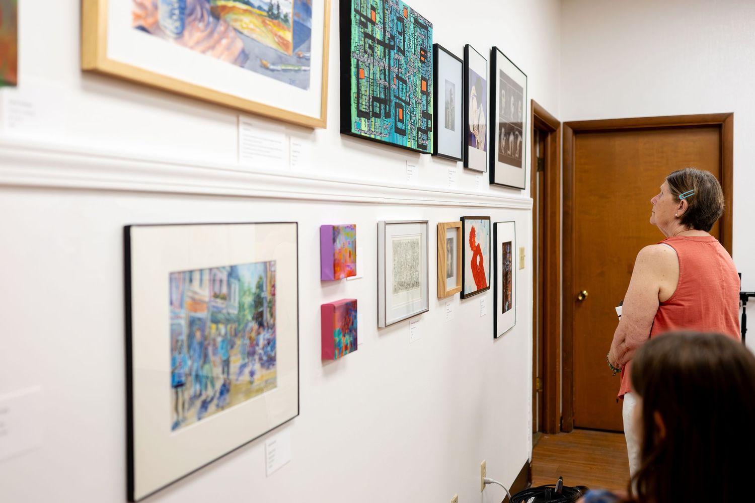 Woman viewing colorful artwork and paintings displayed on white gallery walls during an art exhibition.