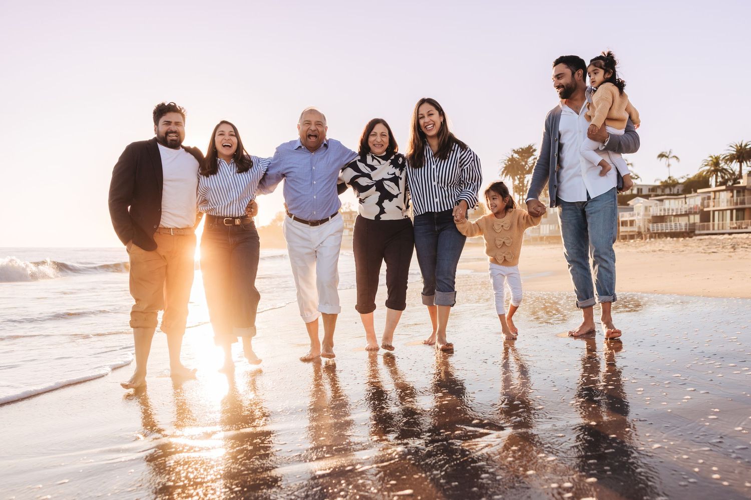 A group of people walking together along a beach at sunset with waves splashing at their feet.