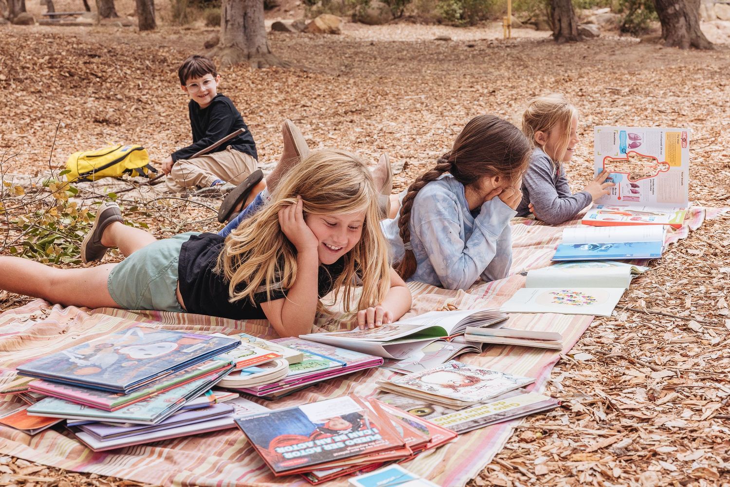 Students lying on blankets reading books together outdoors in a natural setting.