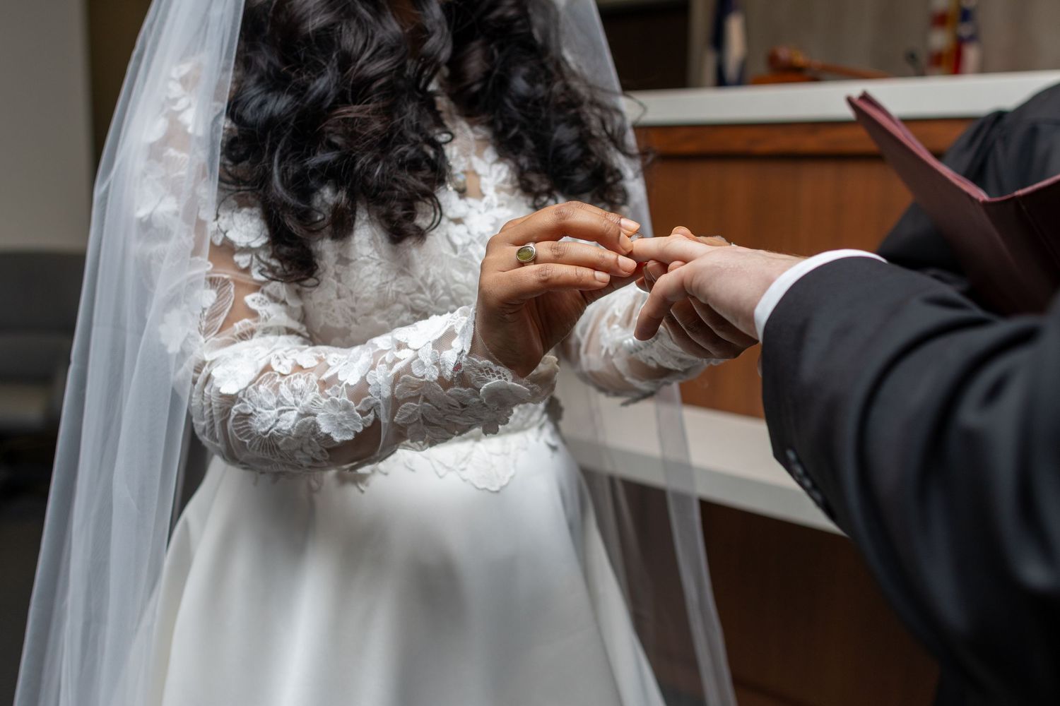 Groom placing a wedding ring on bride's finger during a church ceremony, bride wearing lace dress and veil.