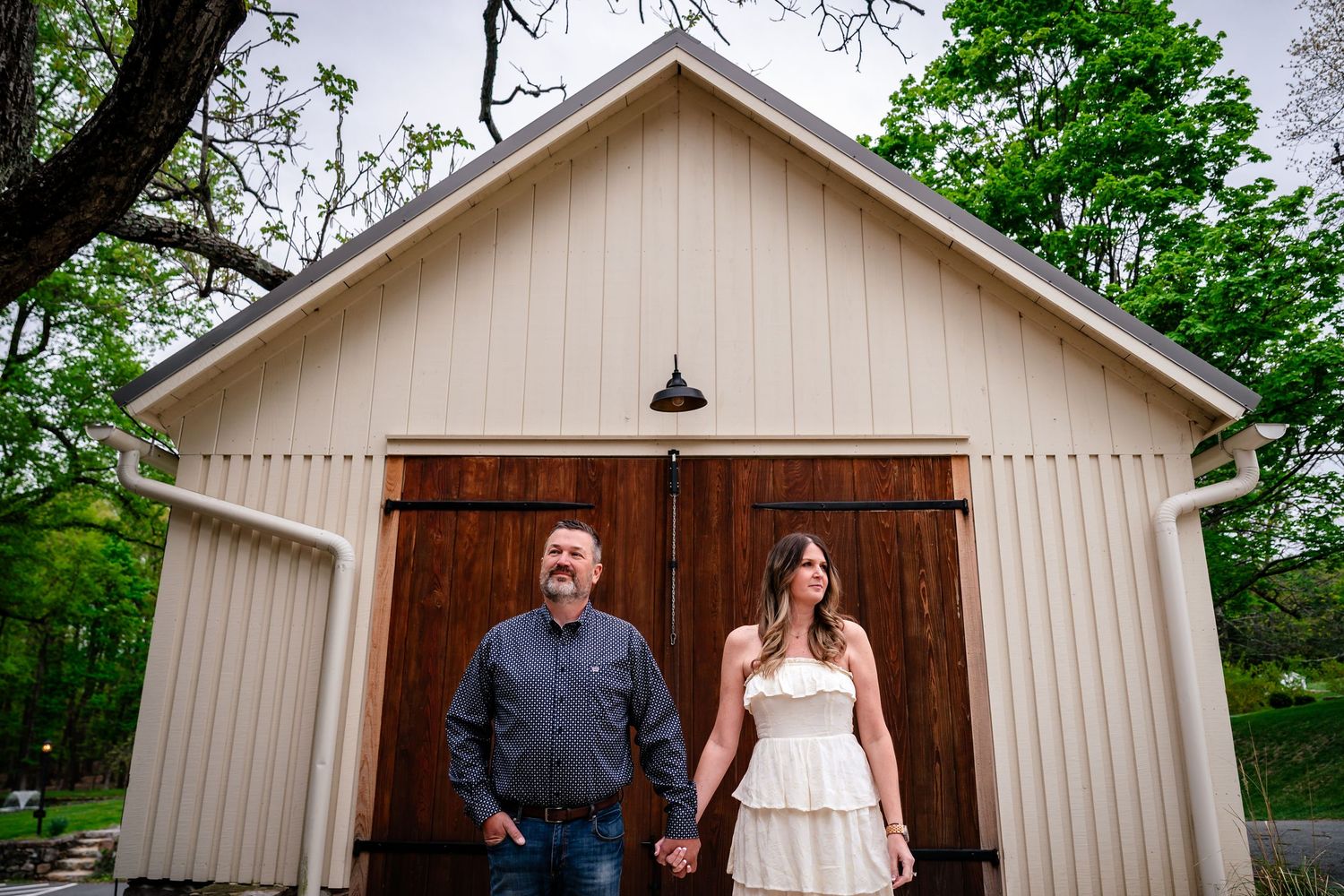 Couple holding hands in front of a rustic barn with wooden doors at an outdoor wedding venue.