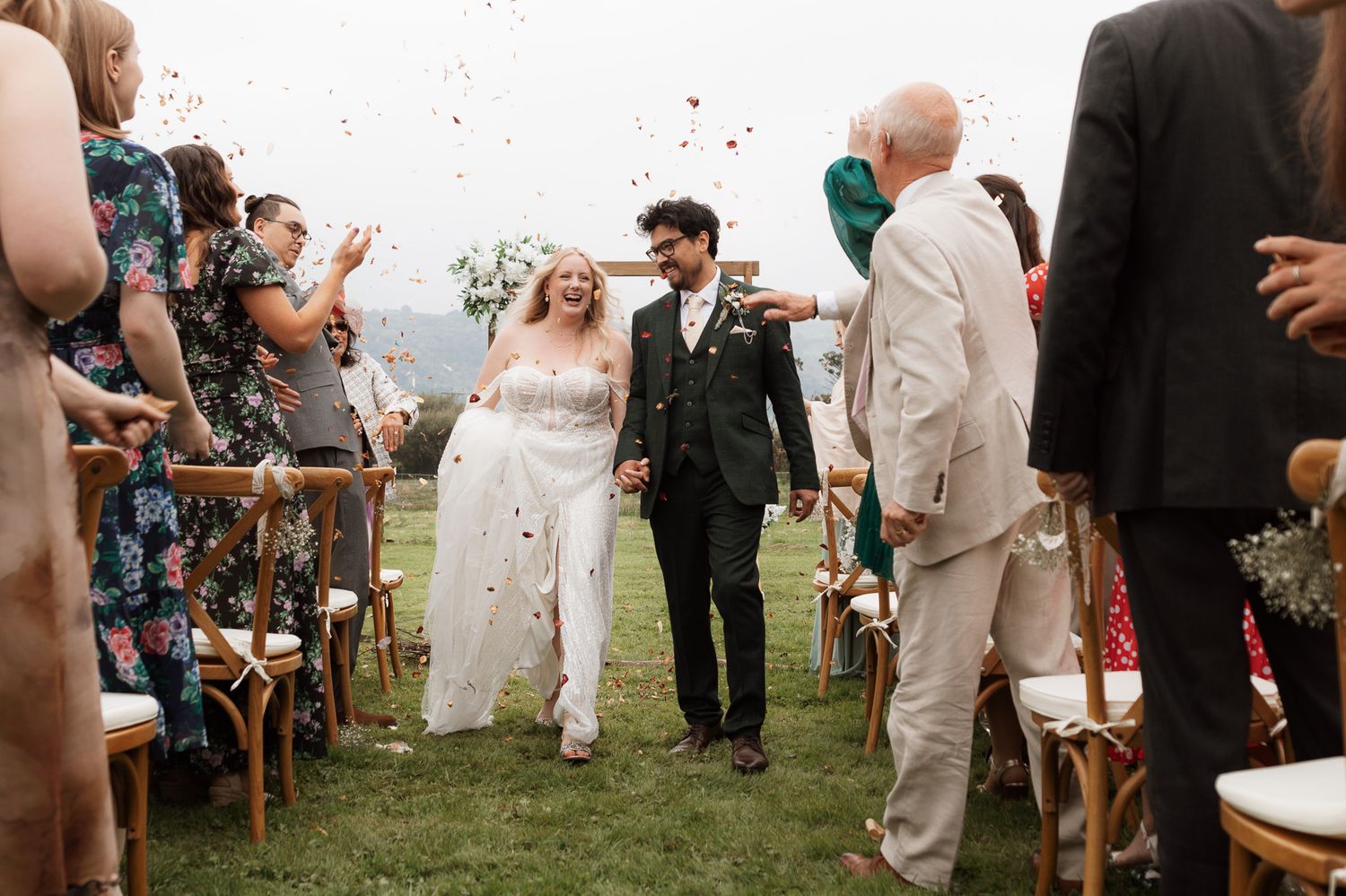 Wedding couple showered by dried rose petal confetti thrown by guests after Welsh mountain outdoor venue ceremony at Blue Acre Weddings.
