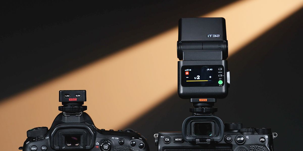Two professional mirrorless cameras with external flash units mounted on hot shoes, displayed on a warm brown gradient background.