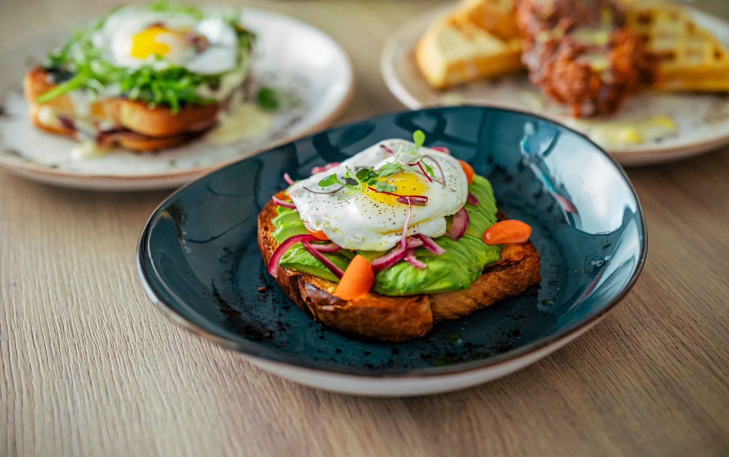 Sunny side up eggs served on various dishes with colorful garnishes and toppings on wooden table surface.