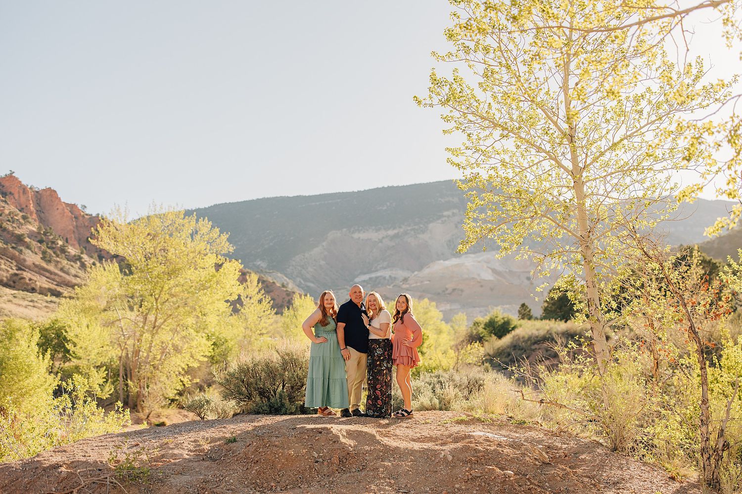 Family posing outdoors in Colorado mountains surrounded by autumn trees and red rock formations in warm sunlight.