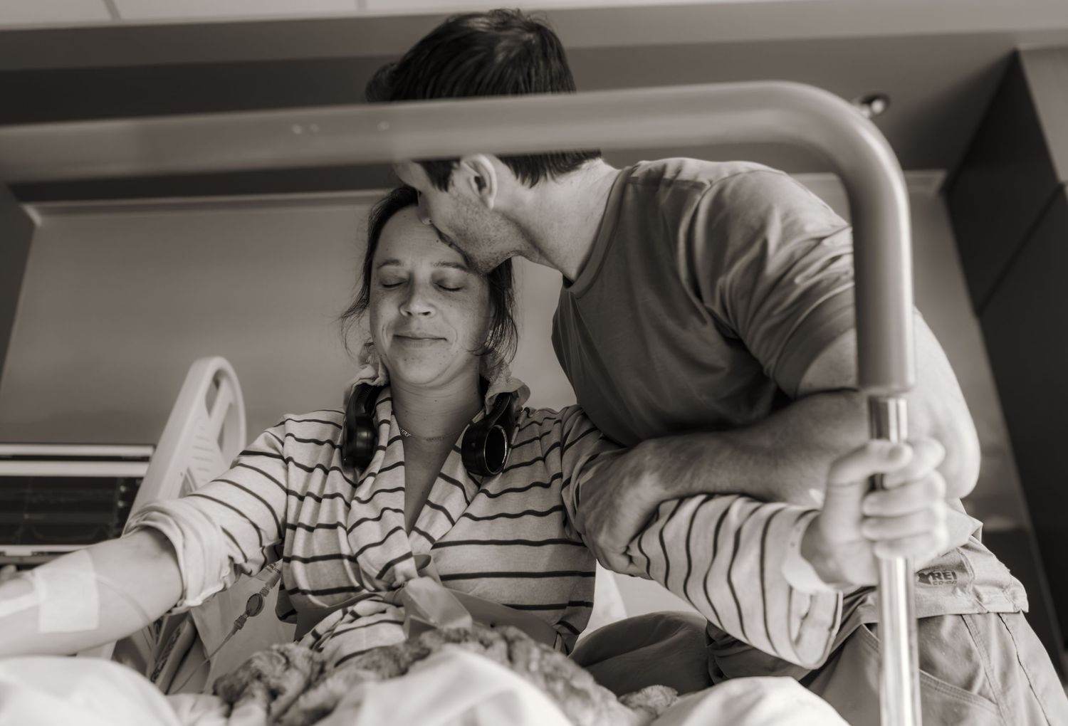 Black and white photo of a man kissing a woman's forehead in a hospital bed during childbirth.
