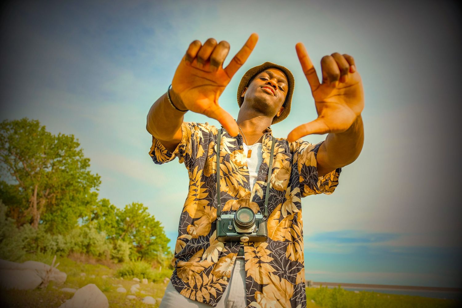 A person wearing a camouflage shirt raises their arms joyfully against a blue sky and green trees background.