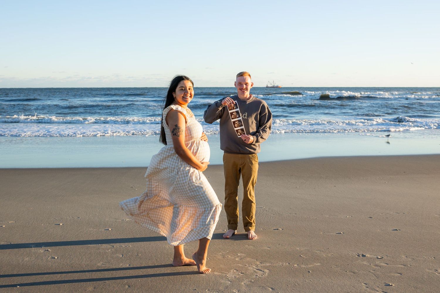 Pregnant mother in a flowing neutral dress standing on the beach at sunset in Emerald Isle, NC during a maternity photography session