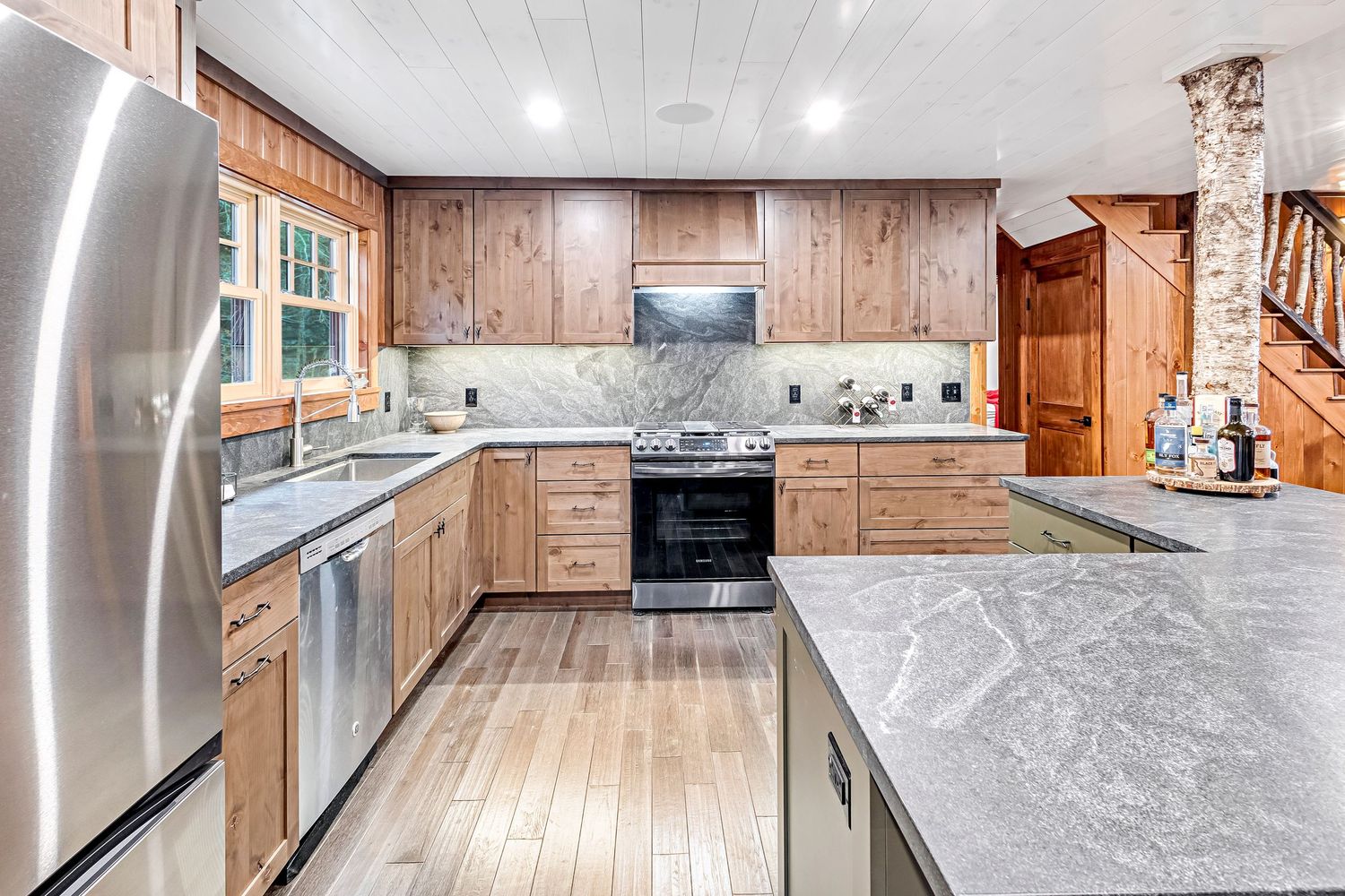 Modern U-shaped kitchen with light wood cabinets, stainless steel appliances and gray marble countertops in rustic style.
