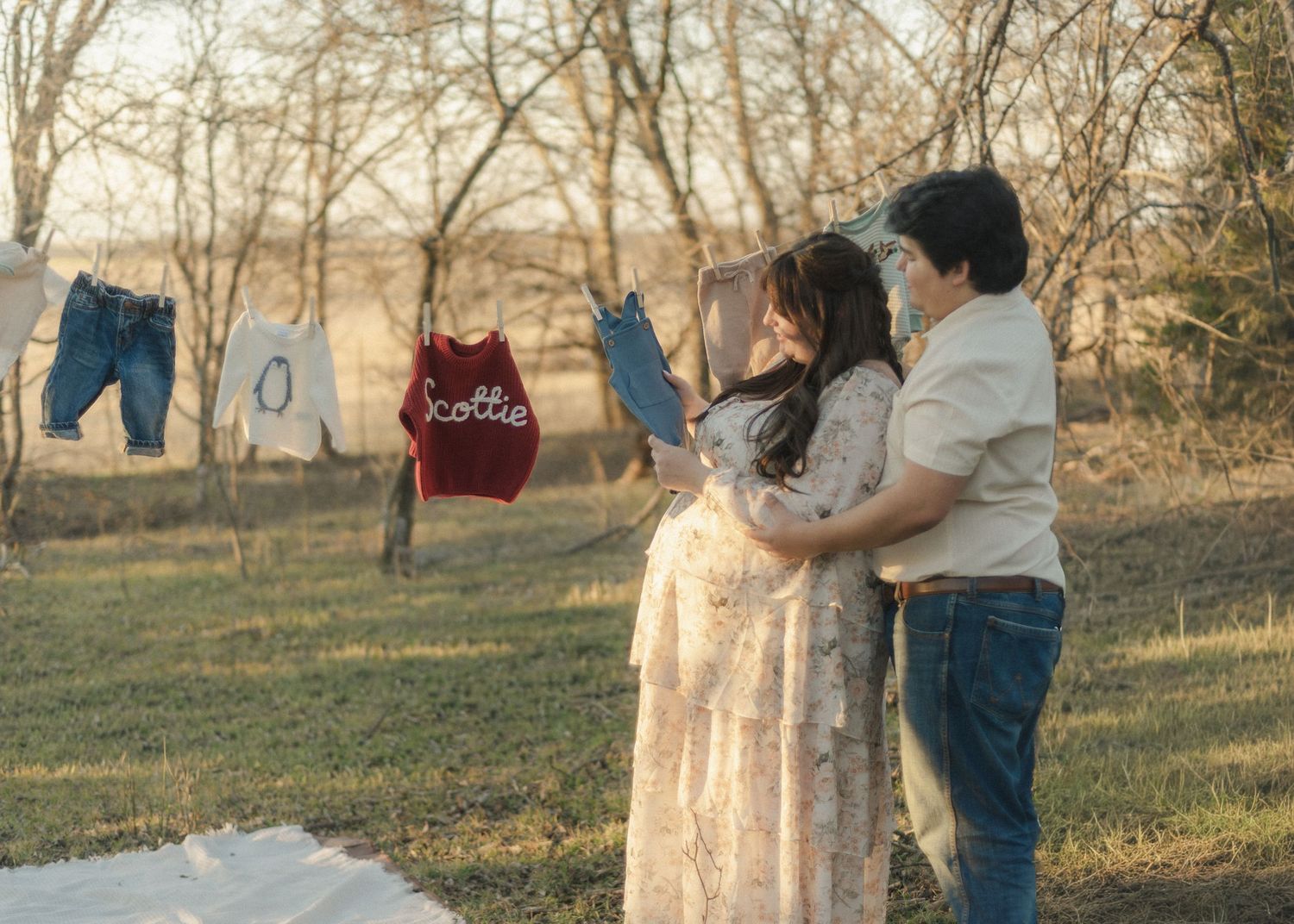 A pregnant Couple look at newborn baby clothing in a field in Troy, Texas for their maternity session.