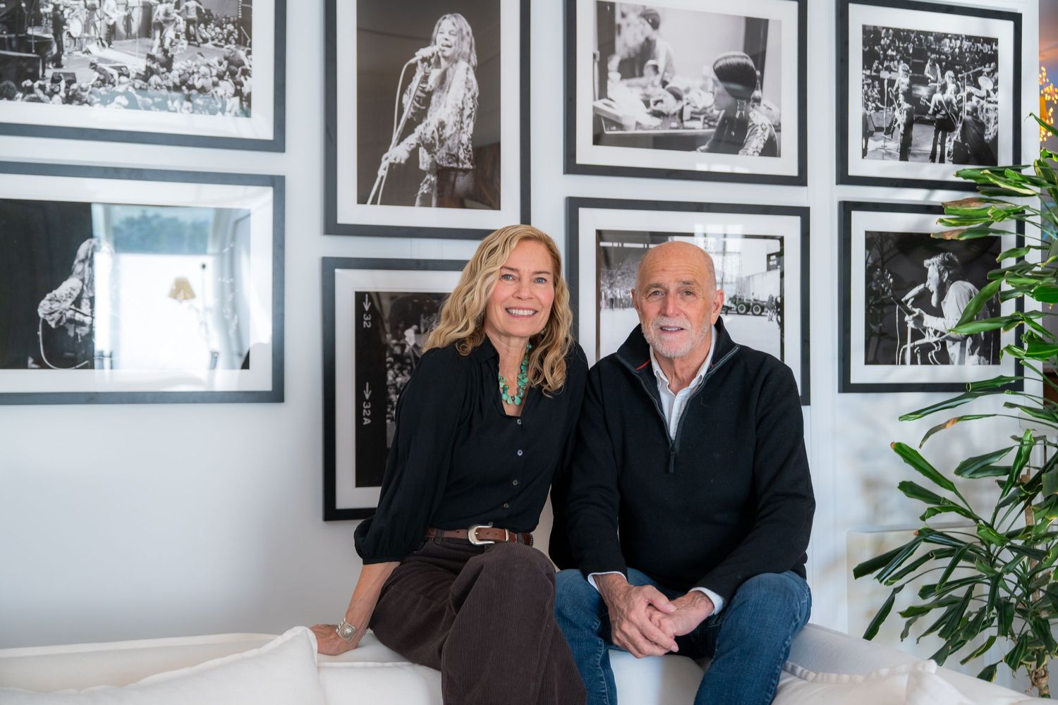 Two people sitting together in front of a gallery wall of black and white rock music photography prints.