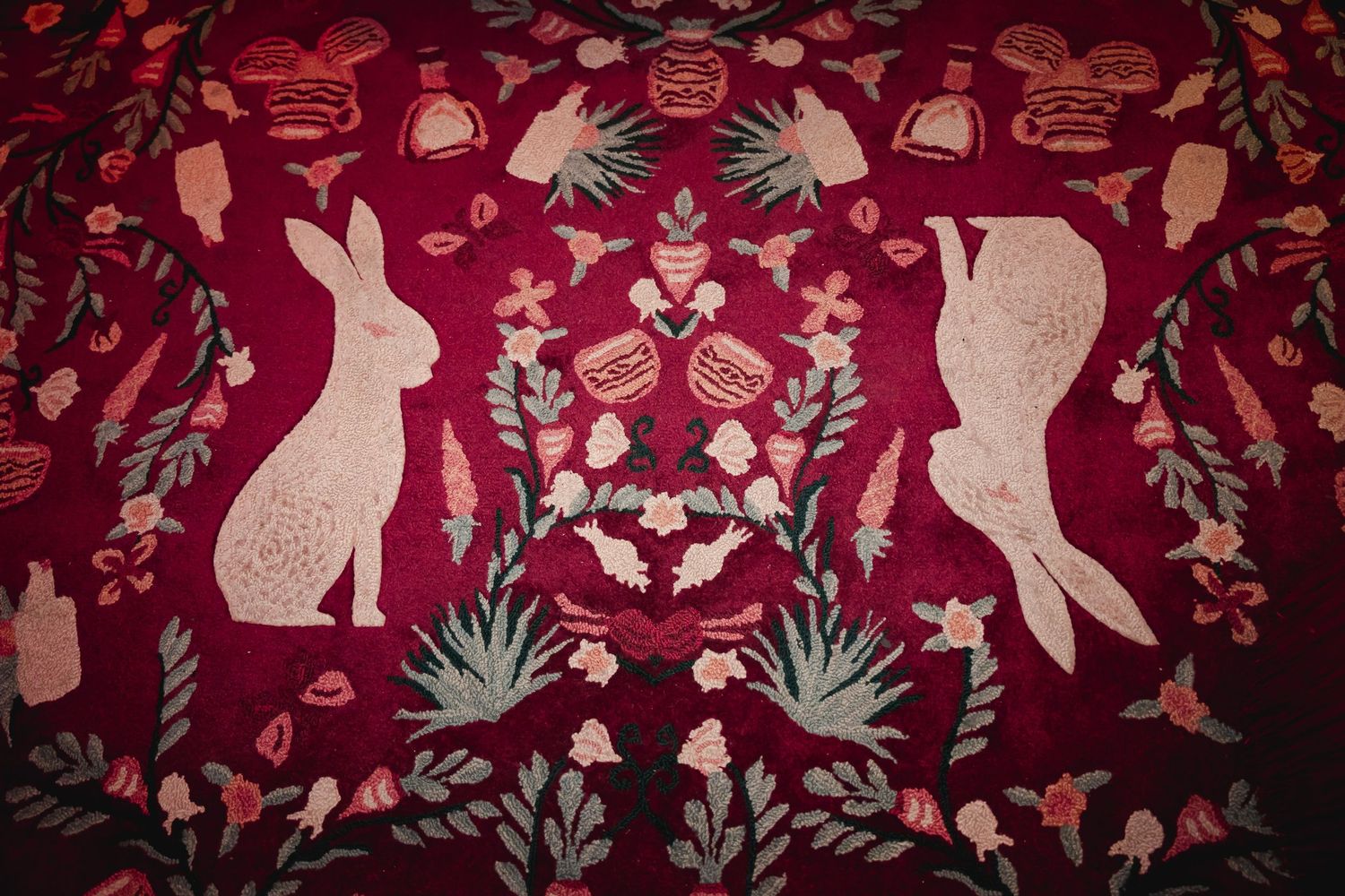 Decorative folk art pattern featuring white rabbits and floral designs against a deep red background.