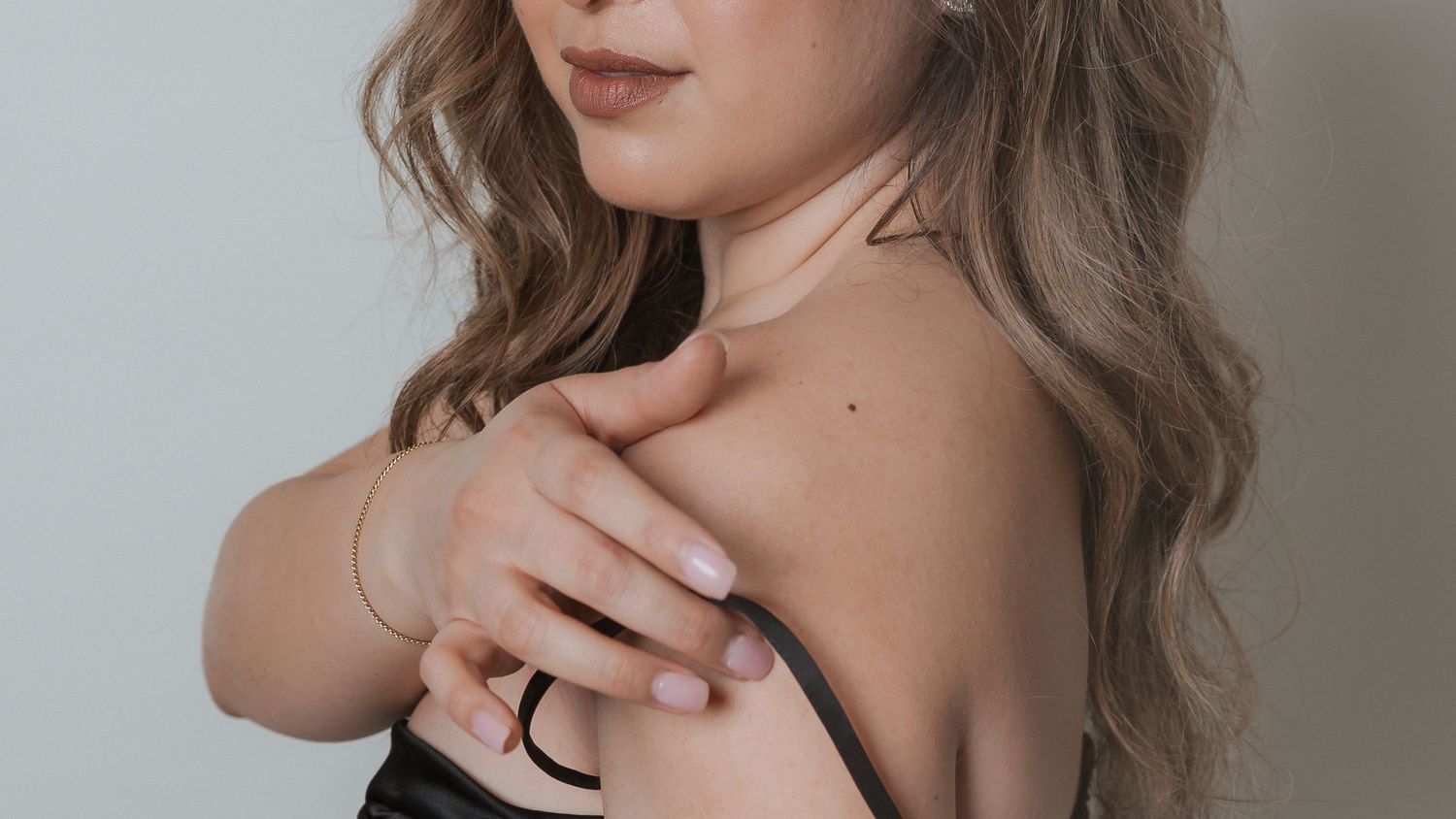 Close-up shot showing jewelry and soft waves of hair against neutral background.