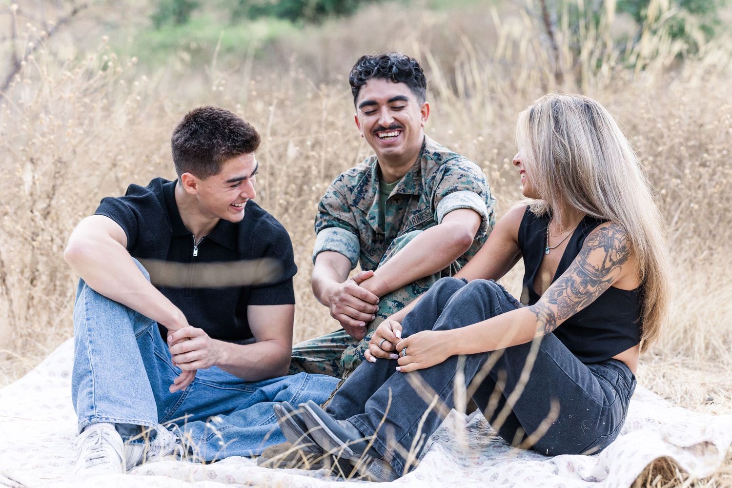 Three friends relaxing together on a blanket in tall grass field.