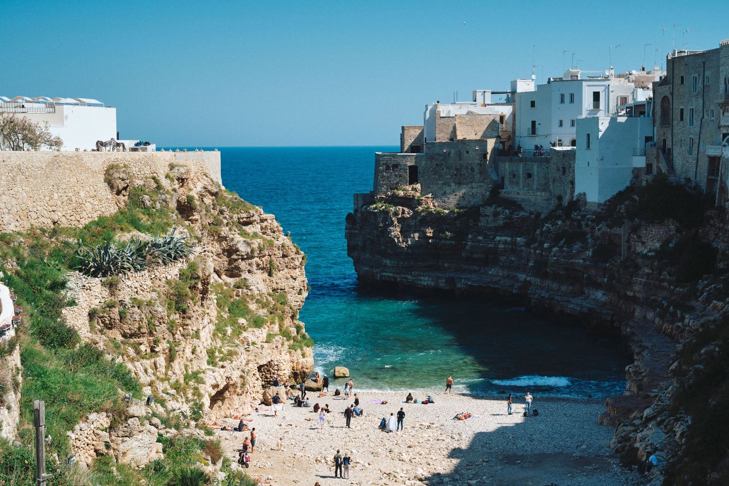 Scenic beach cove surrounded by white buildings and limestone cliffs in coastal Mediterranean town.