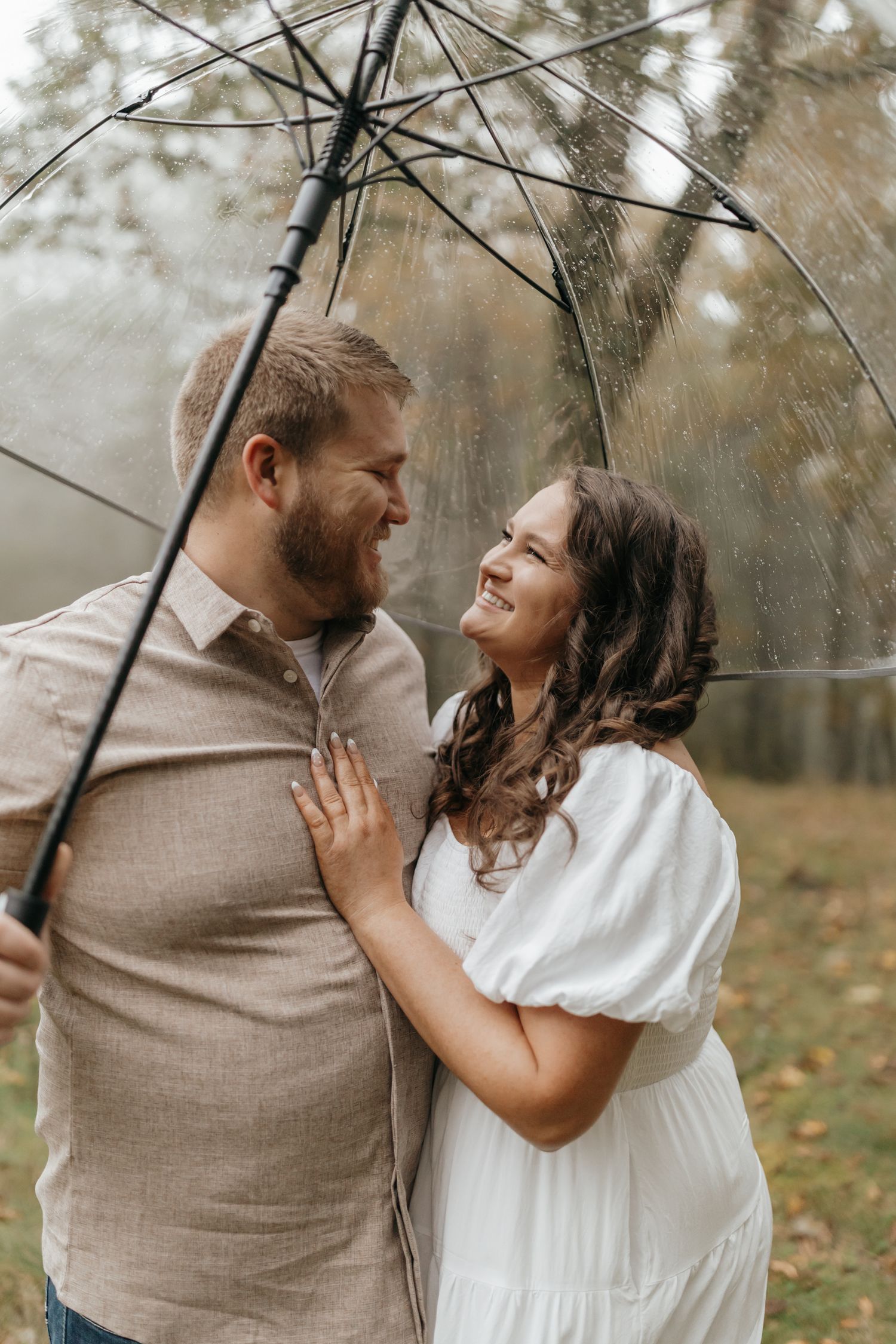 A romantic couple shares a laugh underneath a clear umbrella on a rainy autumn day.