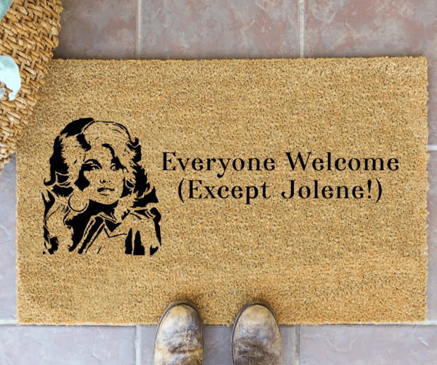 A tan doormat with text reading 'Everyone Welcome (Except Jolene!)' with a vintage illustration design.