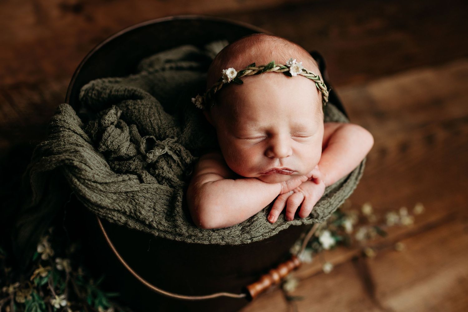 Newborn baby sleeping peacefully in a cozy wool wrap nest during professional photoshoot on wooden backdrop.