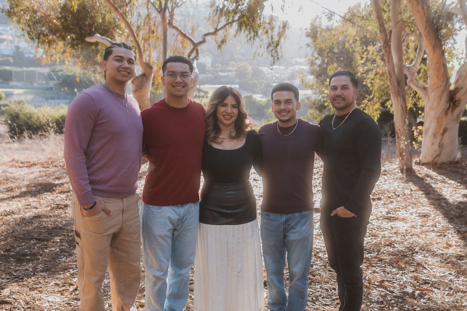A group stands together smiling outdoors in front of eucalyptus trees on a sunny day.