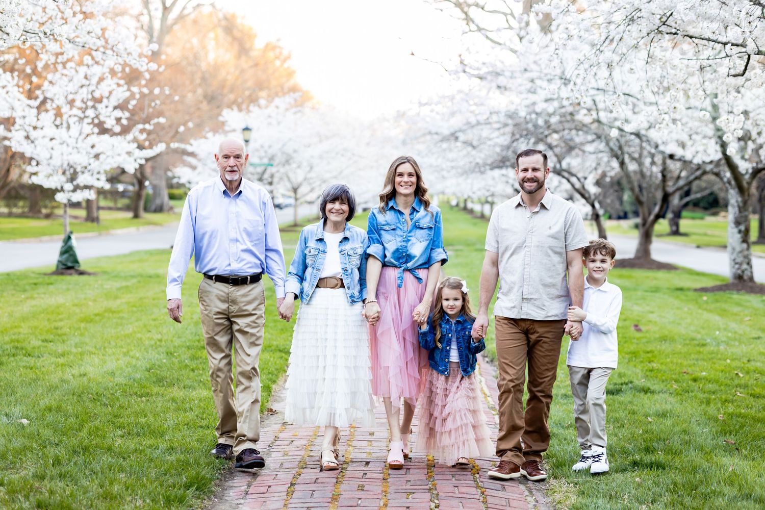 A group walks together along a brick path through a spring garden with blooming trees in the background.