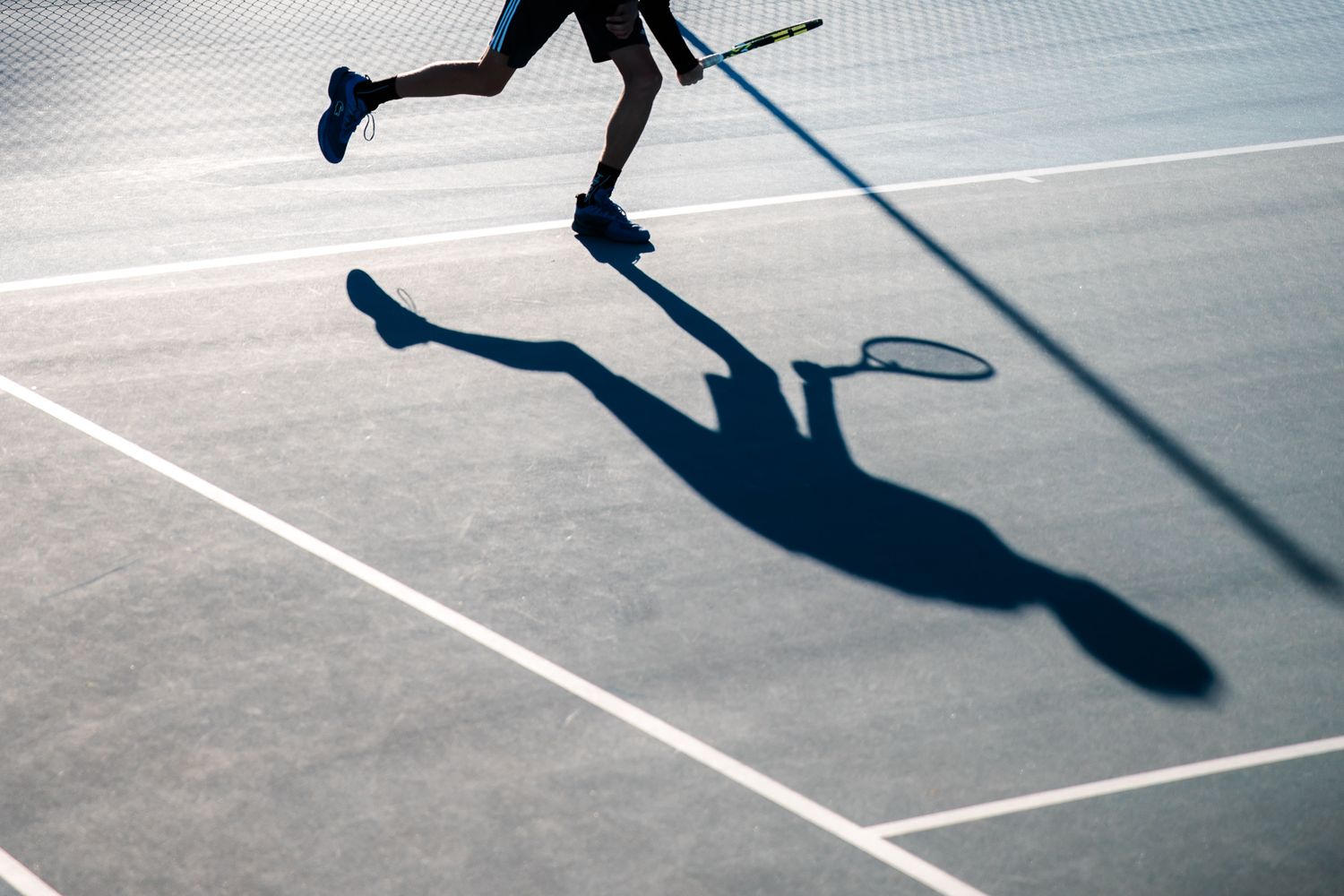 Dramatic shadow cast by tennis player on court making dynamic movement with racquet during match - CCTA - Académie de Tennis en France