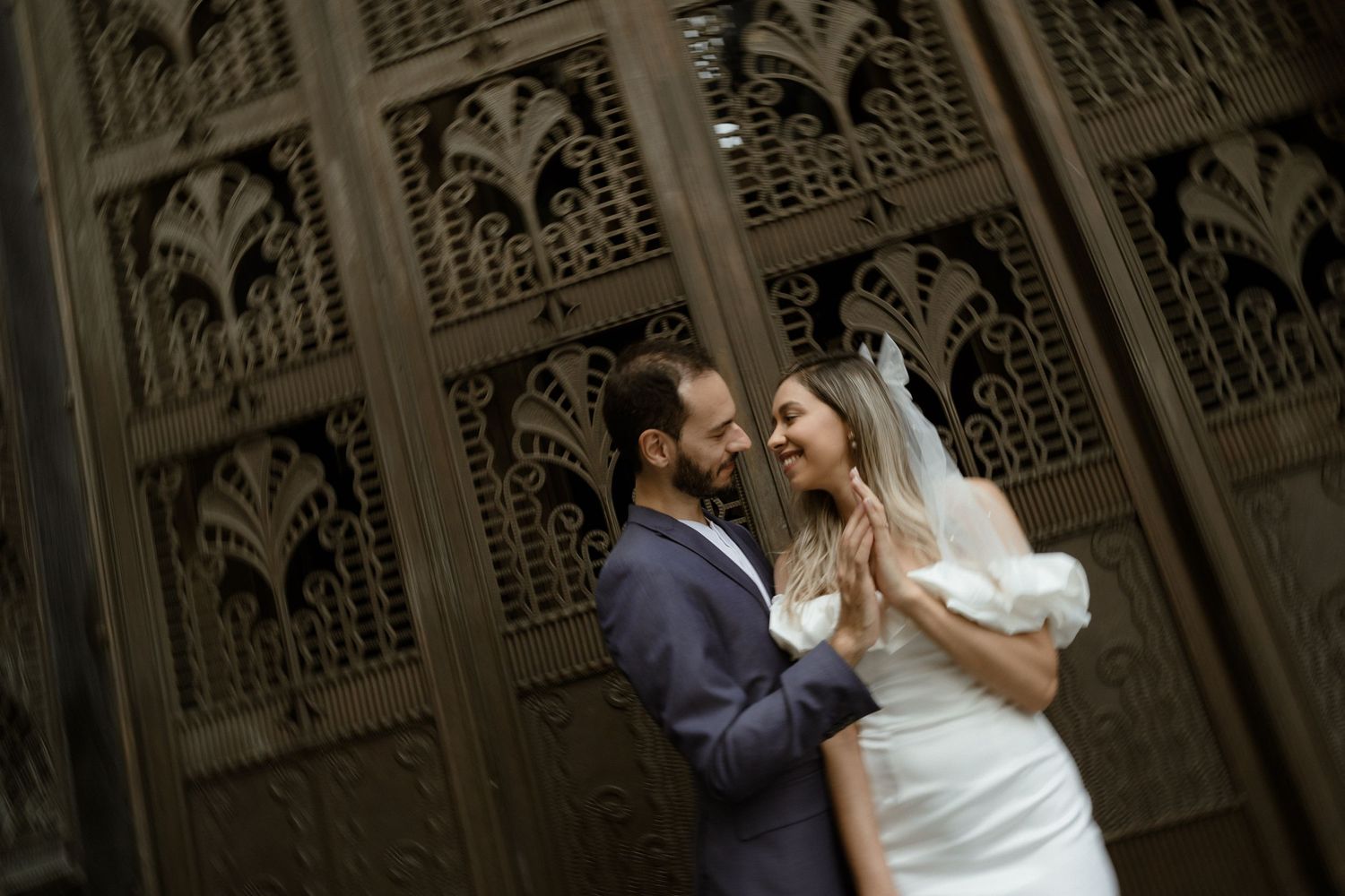 Intimate wedding portrait of couple against ornate gothic architectural background.