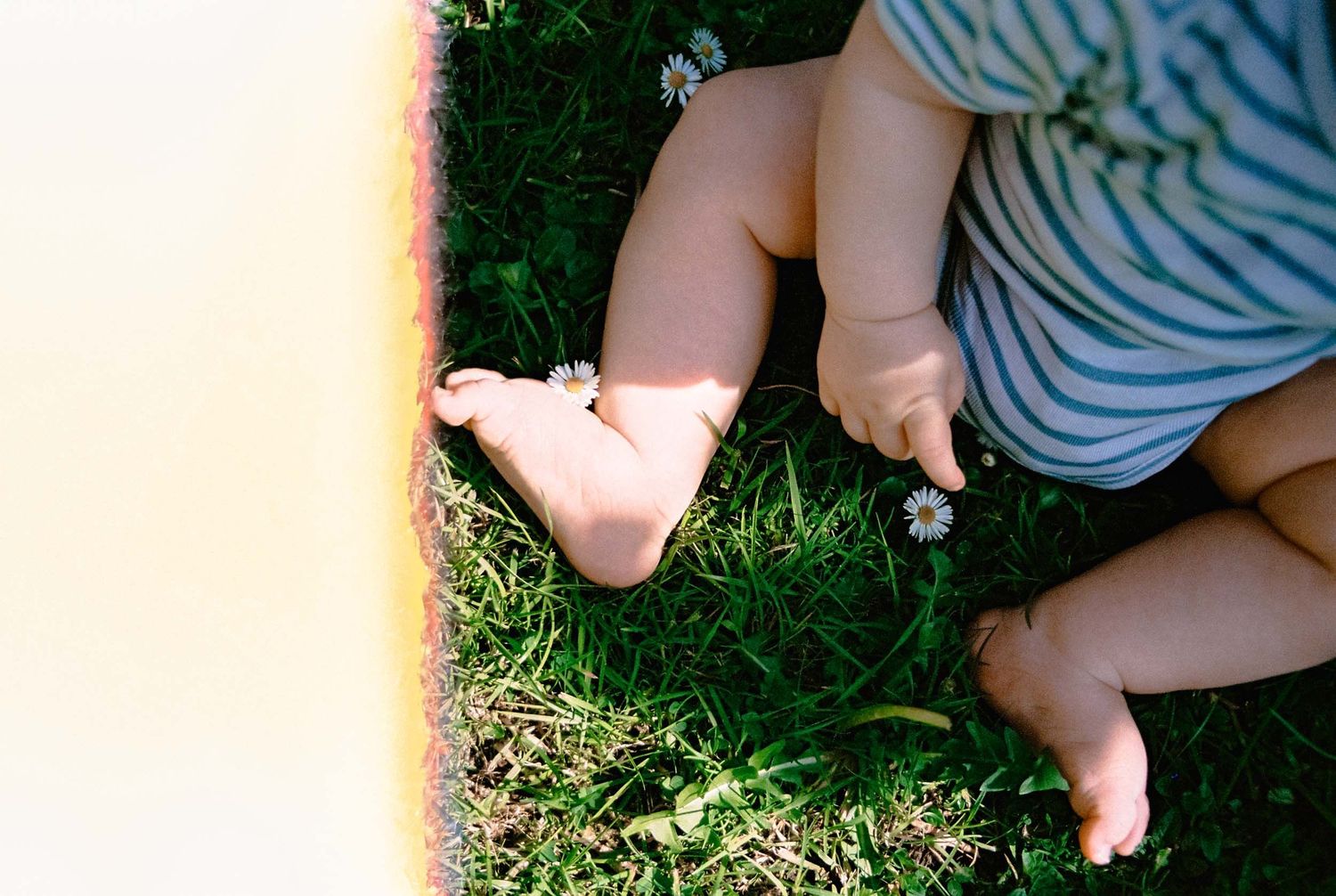 Tiny bare feet and legs of a small child resting on lush green grass in summer sunlight.