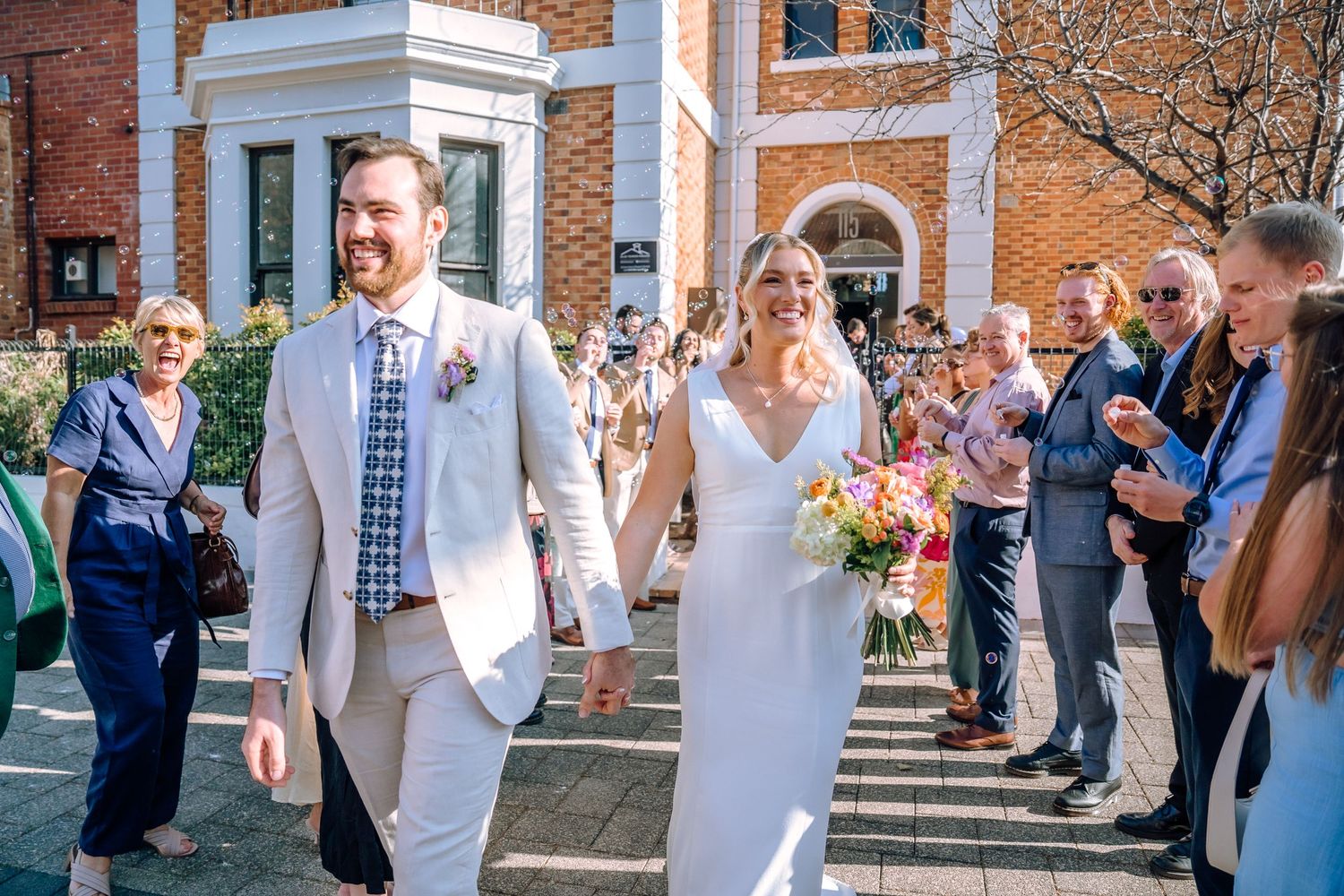 Wedding celebration with guests standing on brick stairs outside an elegant historic building.